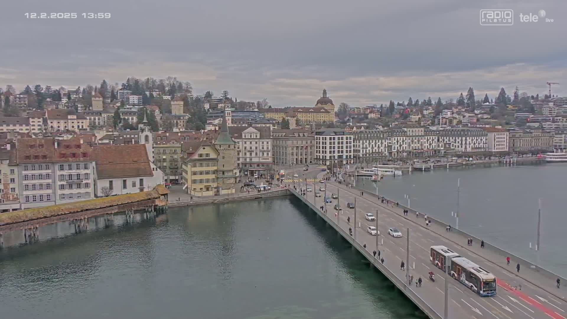 A bridge over a body of water leads to a city of buildings under an overcast sky.
