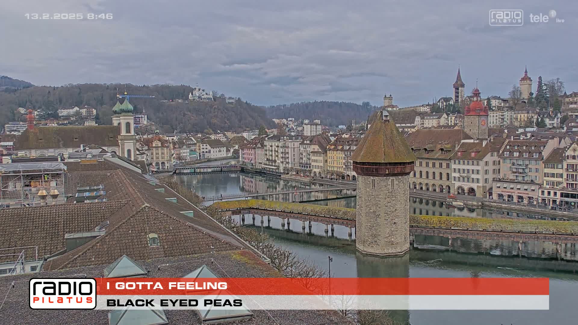An overcast day reveals a European city's waterfront, showcasing a river, bridge, and numerous buildings, including a prominent stone tower.