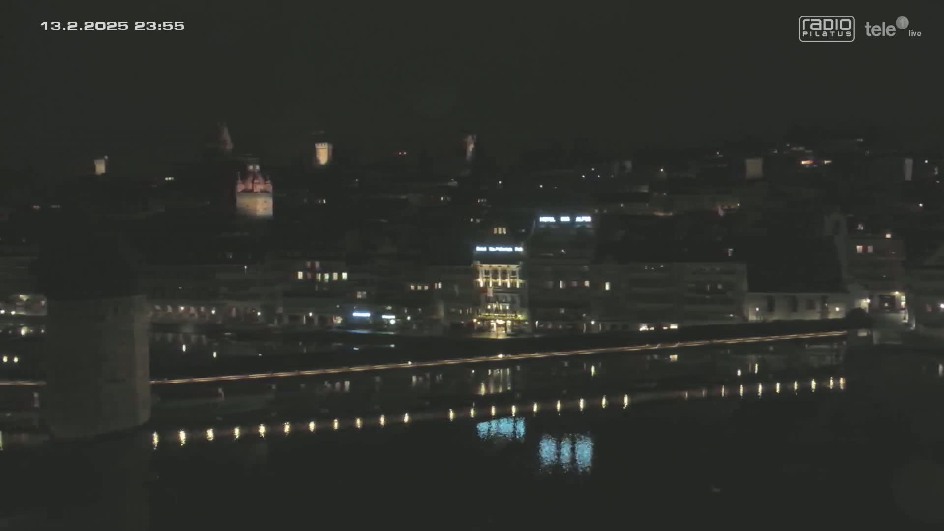 A nighttime, city view shows a body of water reflecting the lights of buildings and a bridge.
