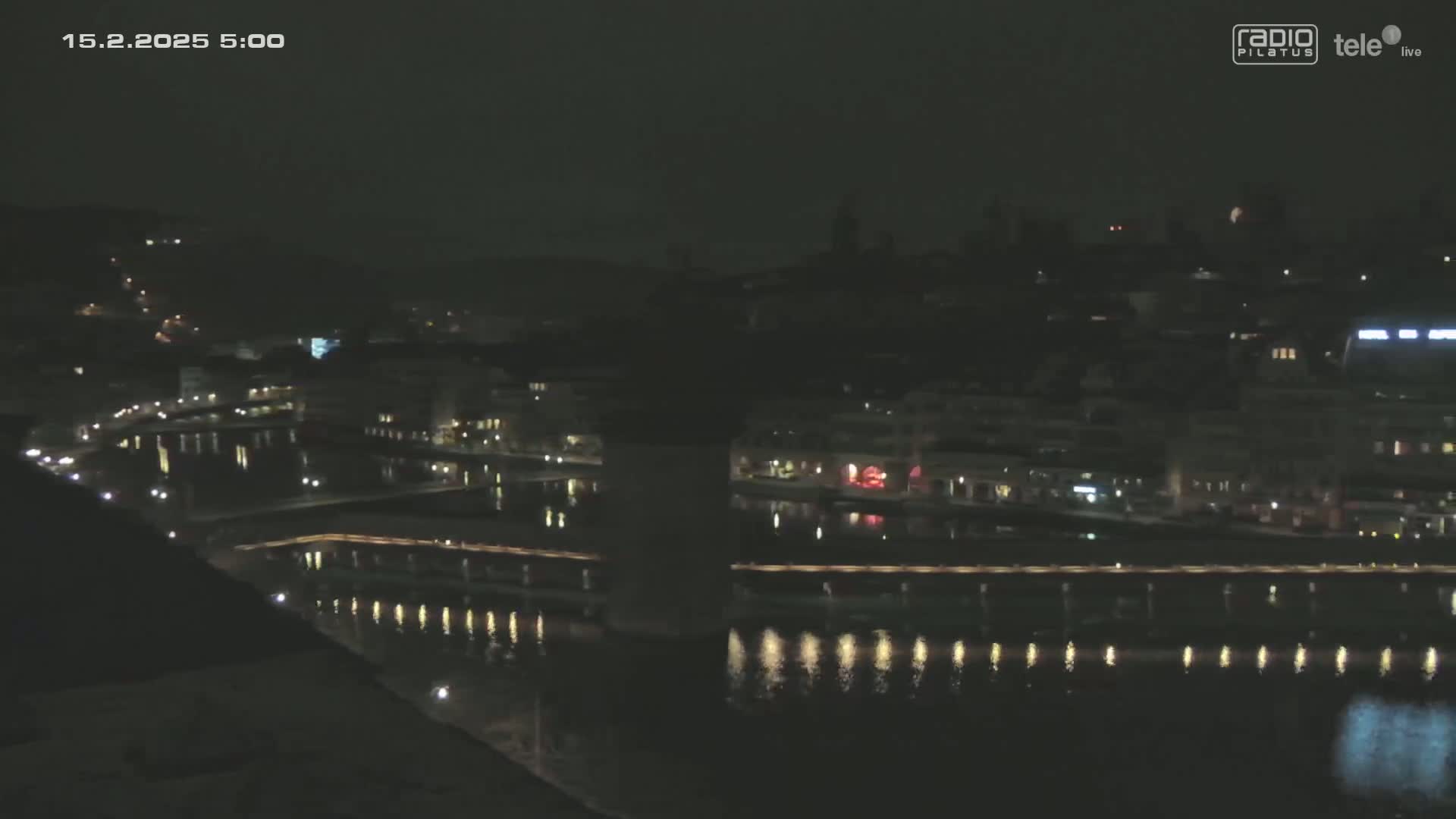 A nighttime, high-angle view of a city with a river reflecting lights, under a dark sky.