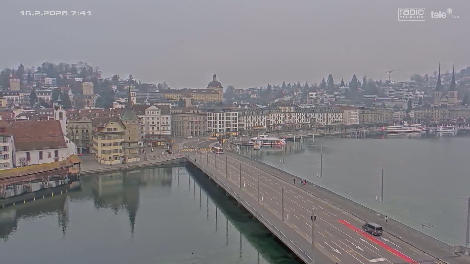A long bridge over calm water leads to a city with many buildings under an overcast sky.