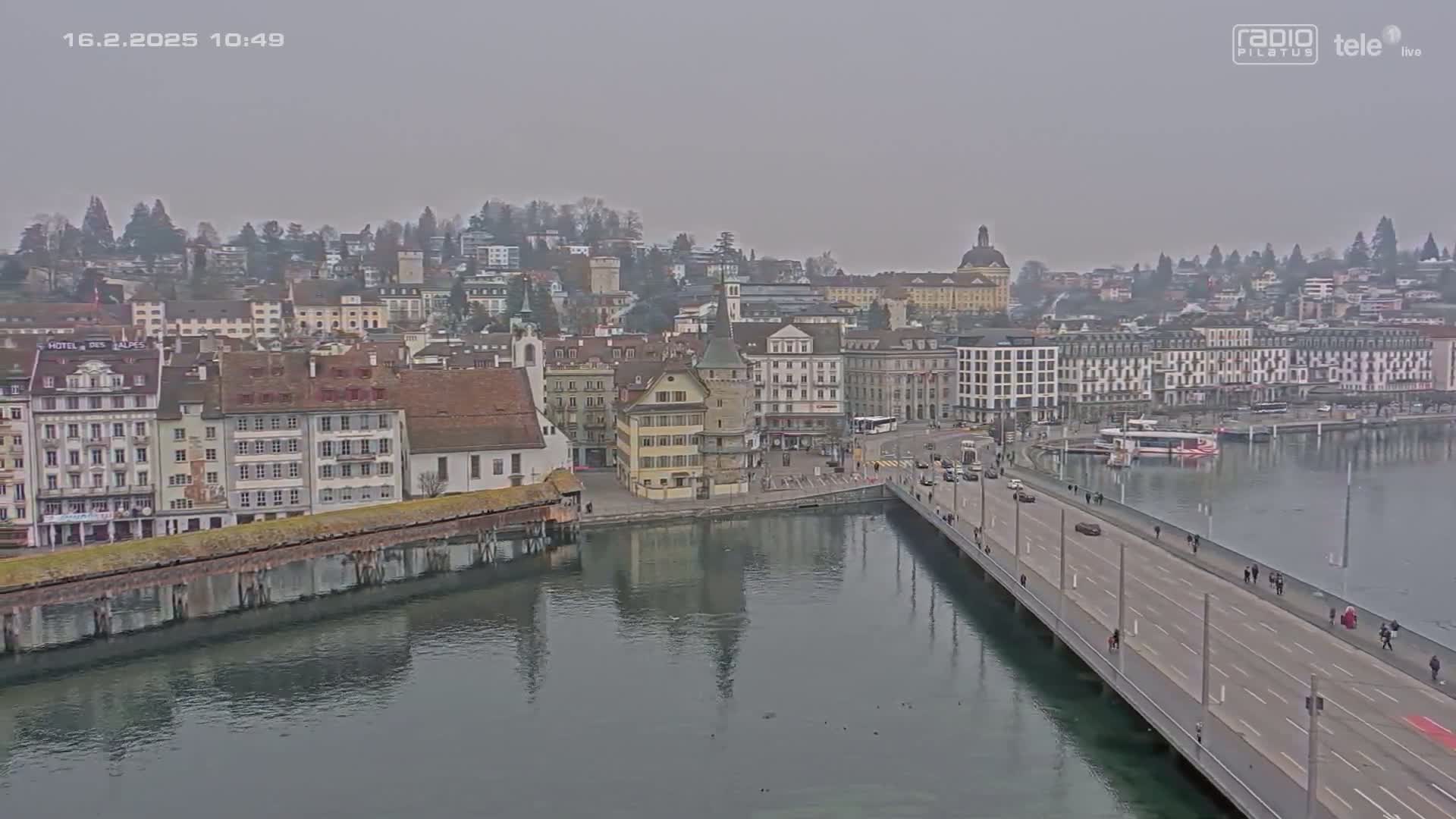 A bridge over a calm river leads to a city of multi-story buildings on a hazy day.