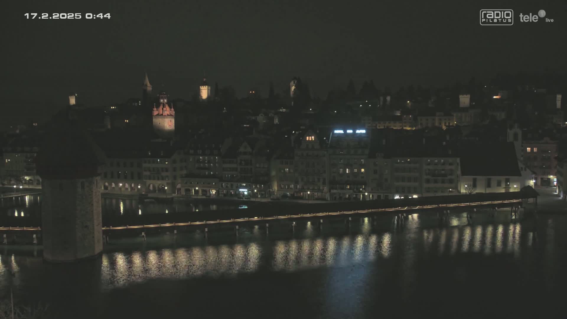 A nighttime view of a town with a bridge spanning a body of water, reflecting lights from buildings and streetlights.