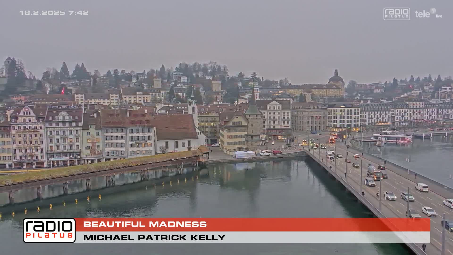 A European city, situated on a river, is overcast with a bridge crossing the water and cars driving across it.