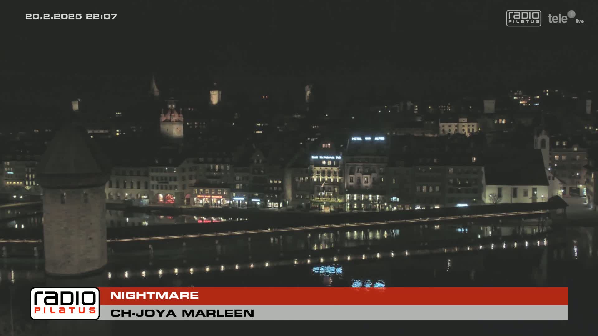 A nighttime view of a city across a body of water, showing illuminated buildings and a stone tower.