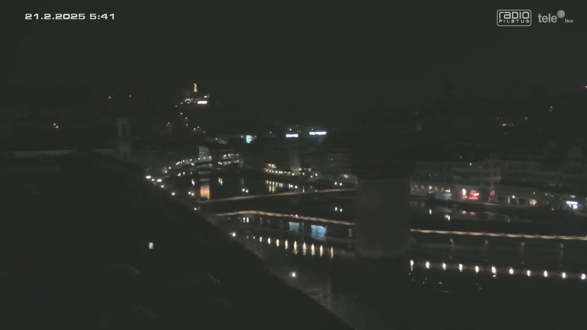 A nighttime long shot of a city with a body of water reflecting the city lights.