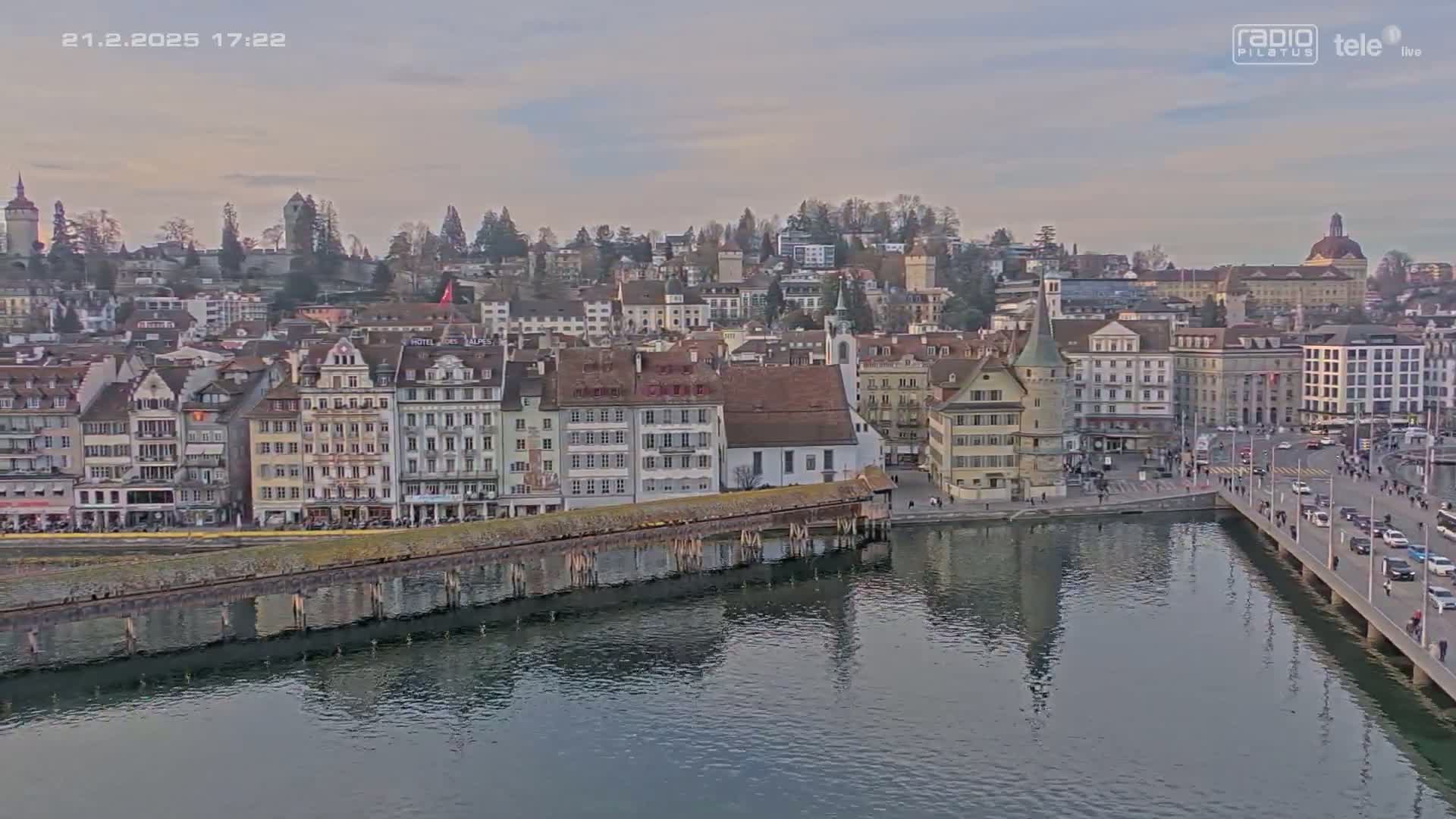 A city with many buildings along a calm body of water under a cloudy sky.
