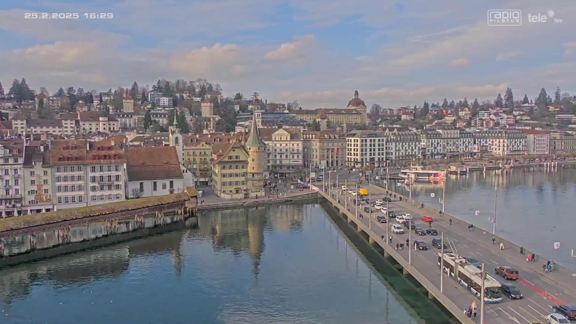 A partly cloudy day reveals a cityscape with a bridge crossing a body of water, lined with buildings, and traffic.