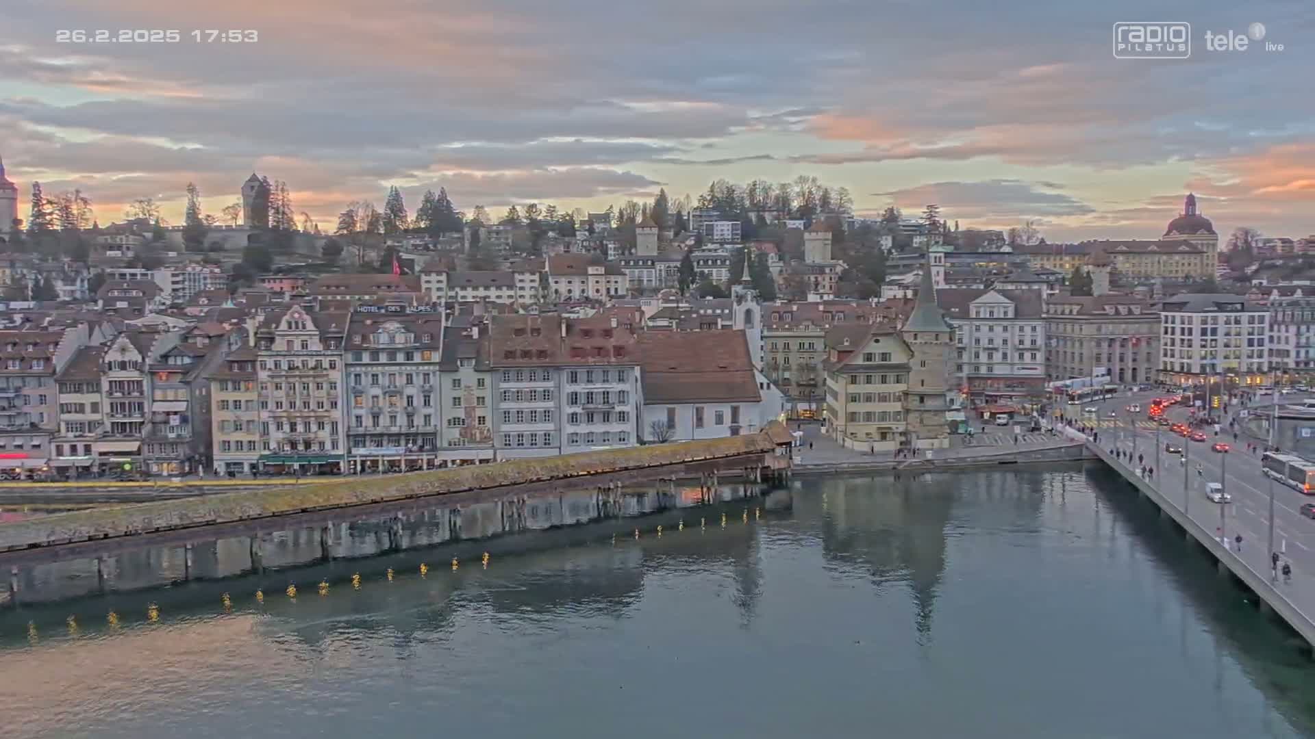 A cityscape with many buildings along a calm body of water under a partly cloudy sunset sky.