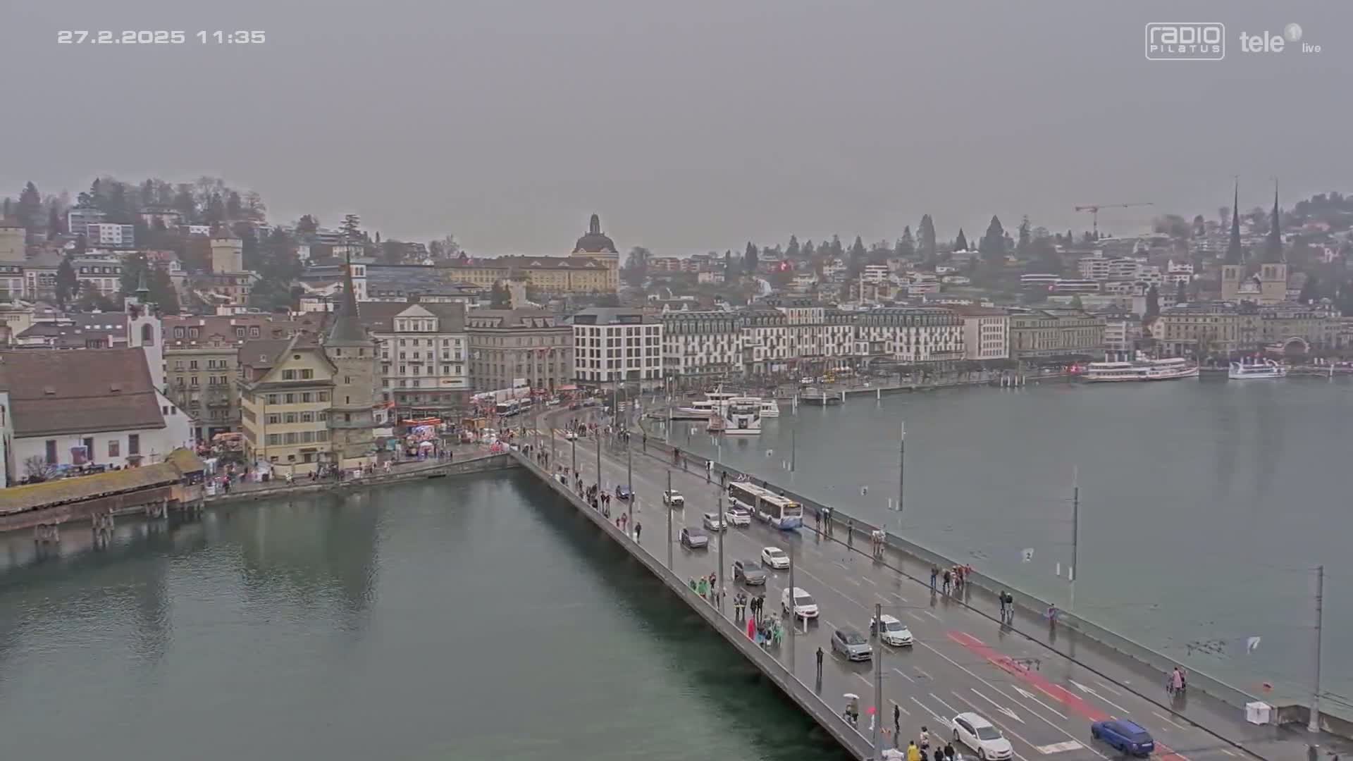 A bridge over a body of water, with a town of buildings in the background, under an overcast sky.