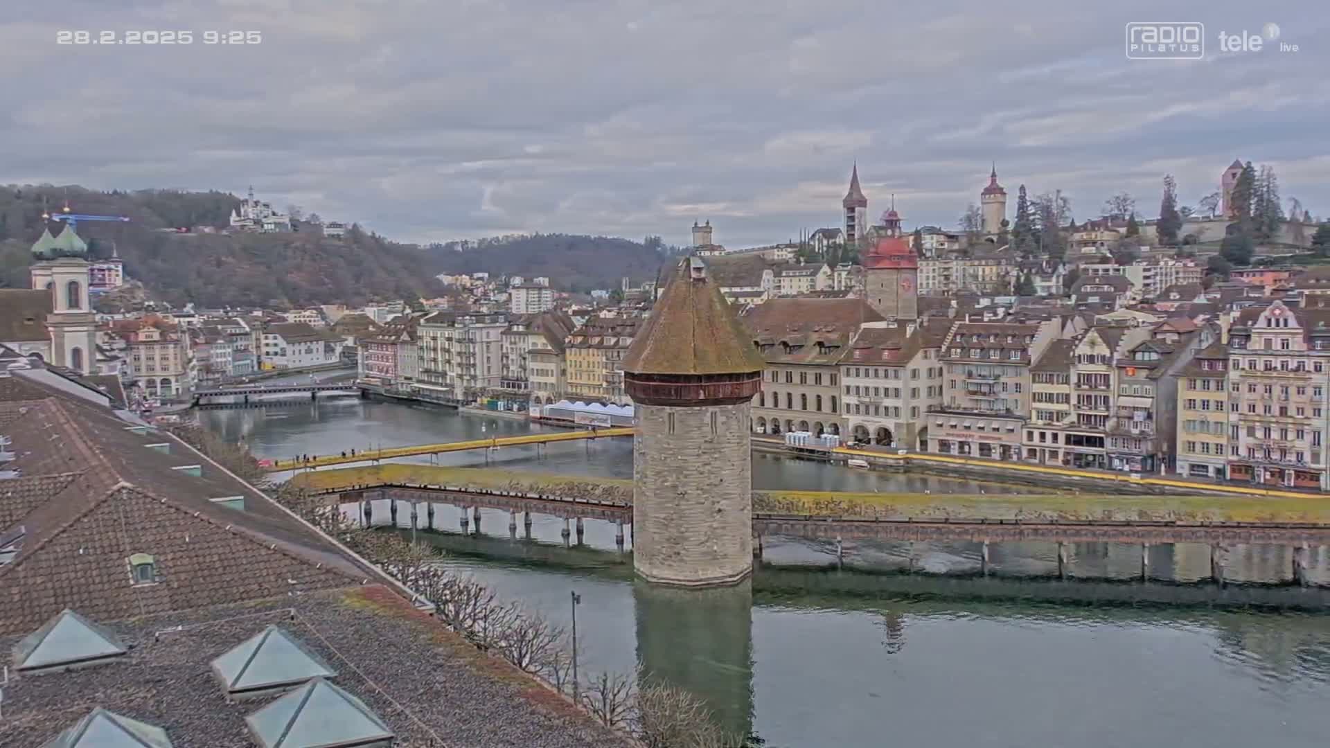 A stone tower stands in a river, surrounded by a city of many buildings under an overcast sky.