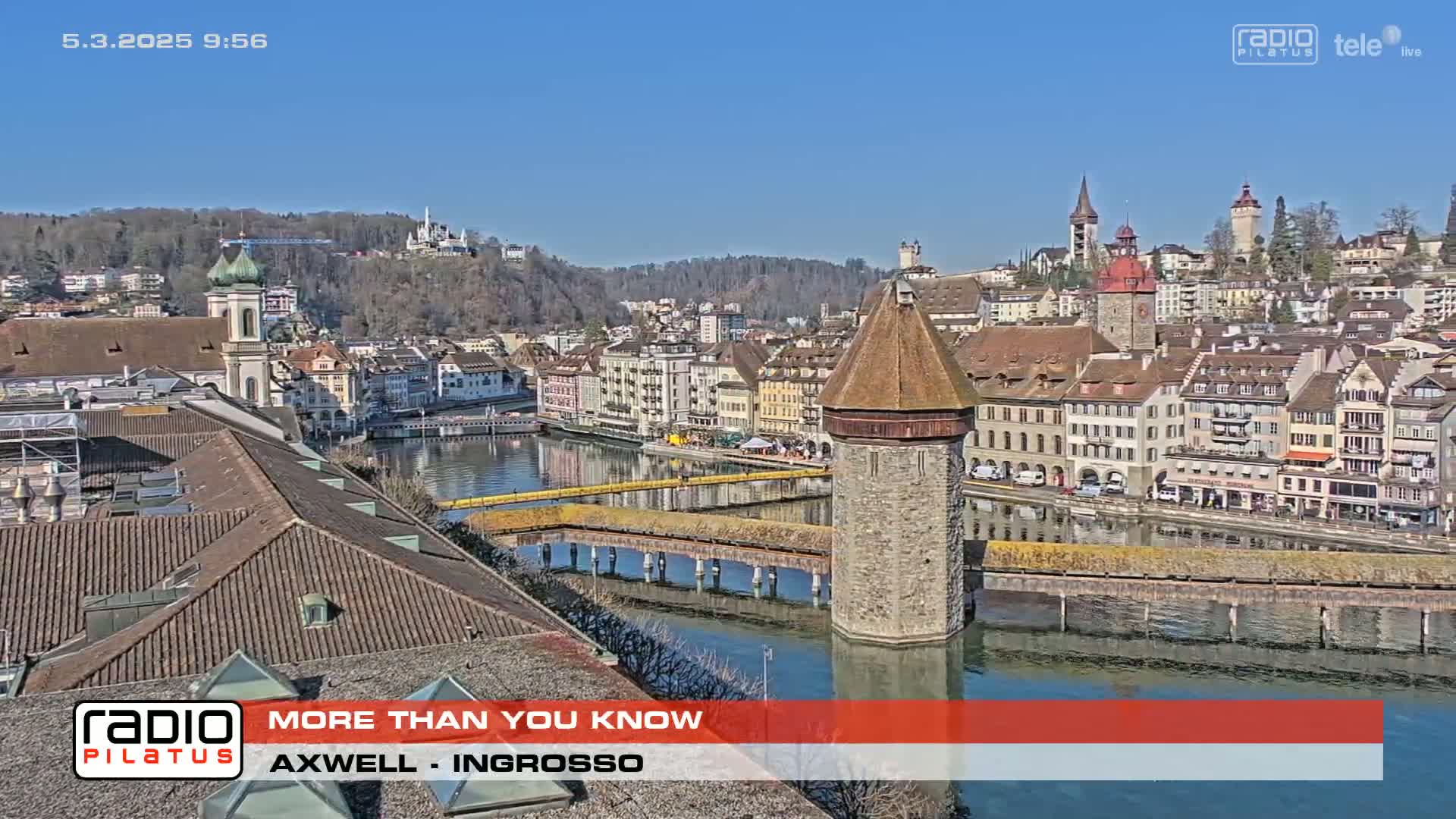 A sunny day reveals a European city with a river, bridge, and numerous buildings, including a prominent tower.