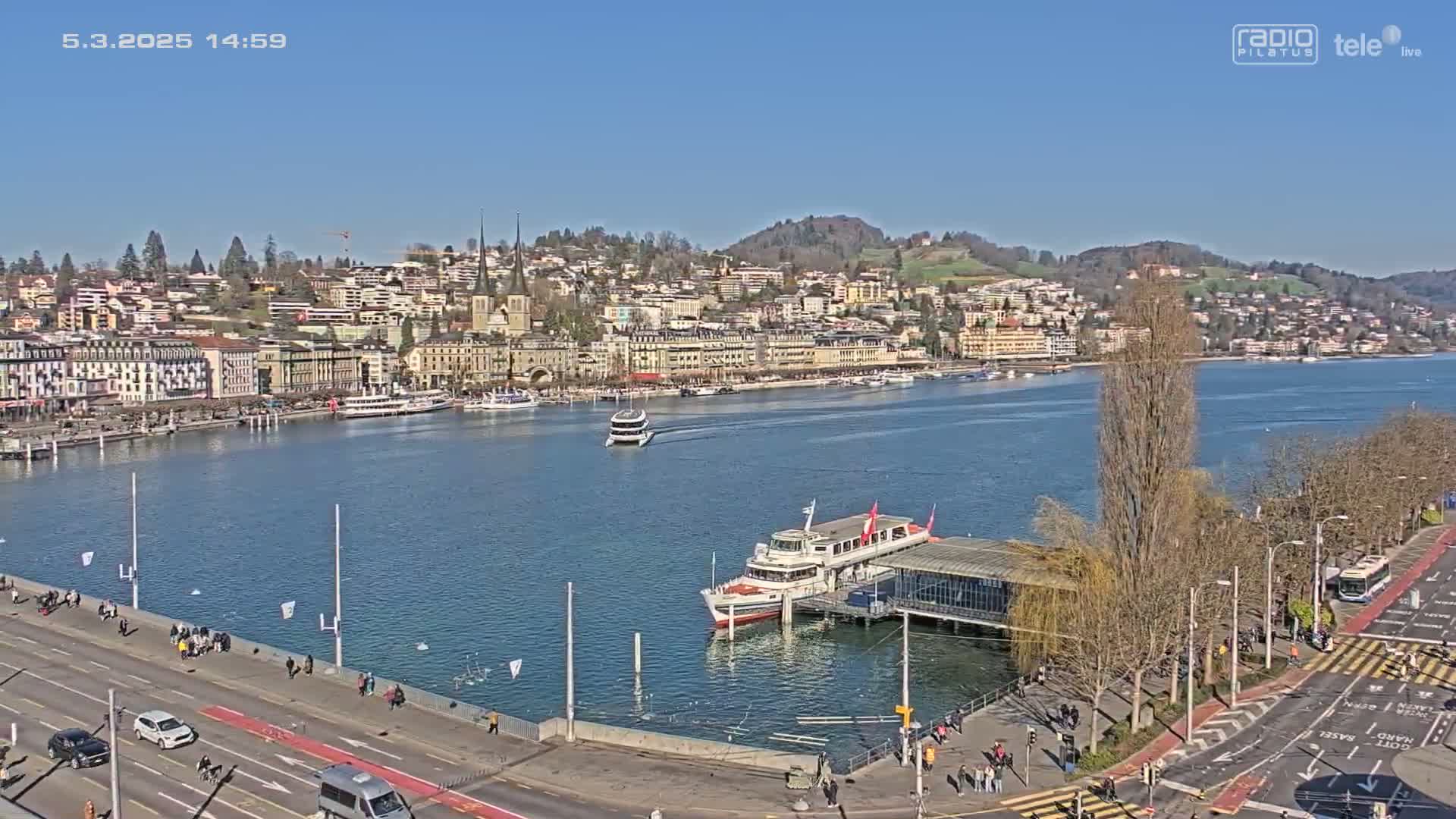 A waterfront city with several buildings and boats on a sunny day, viewed from above.