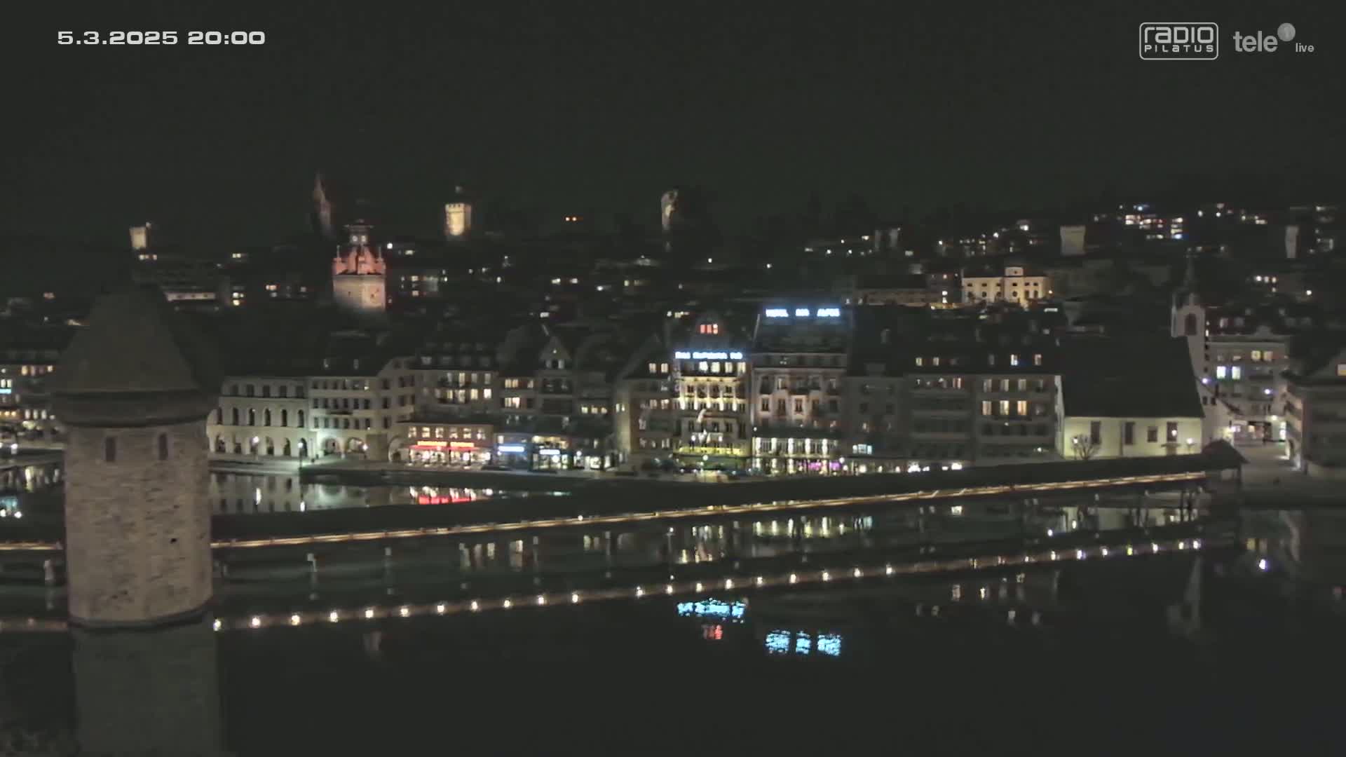 A nighttime view of a city with a body of water reflecting the lights of buildings and a bridge.