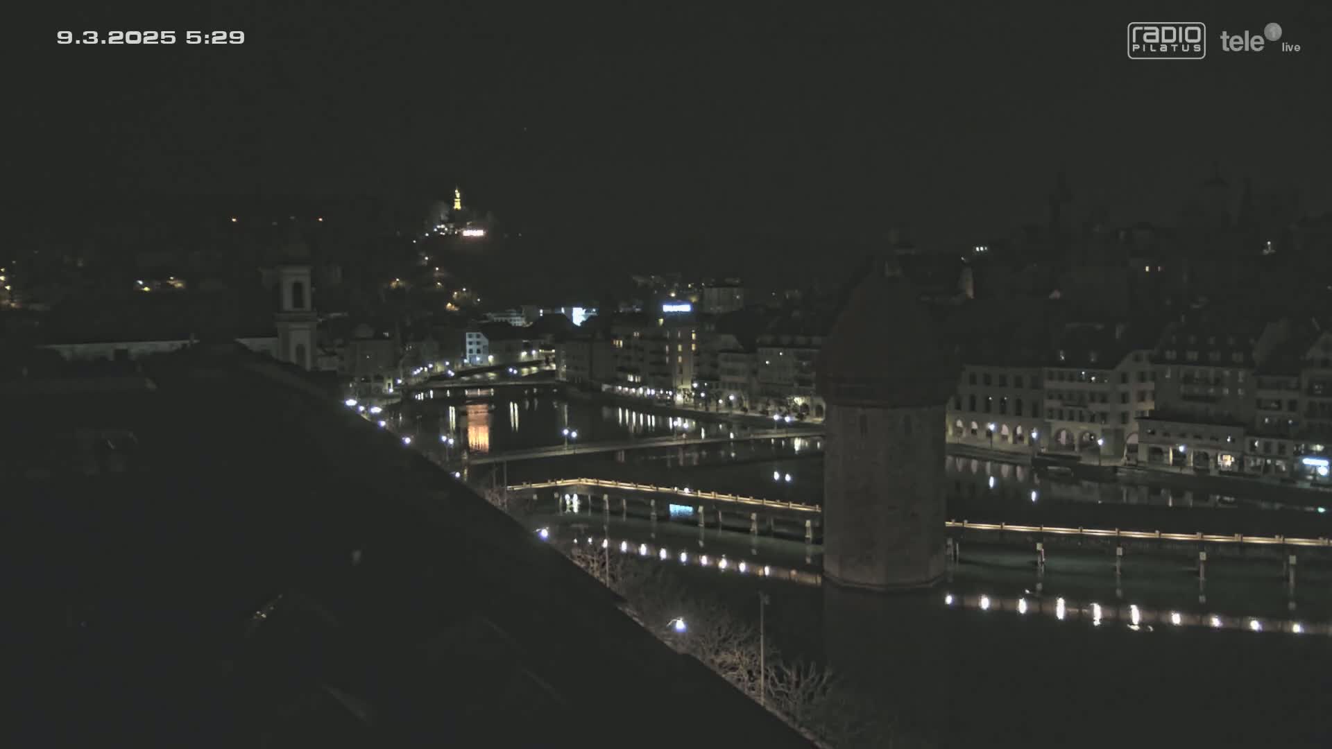 A nighttime view of a city with a river, bridges, and buildings illuminated by lights.