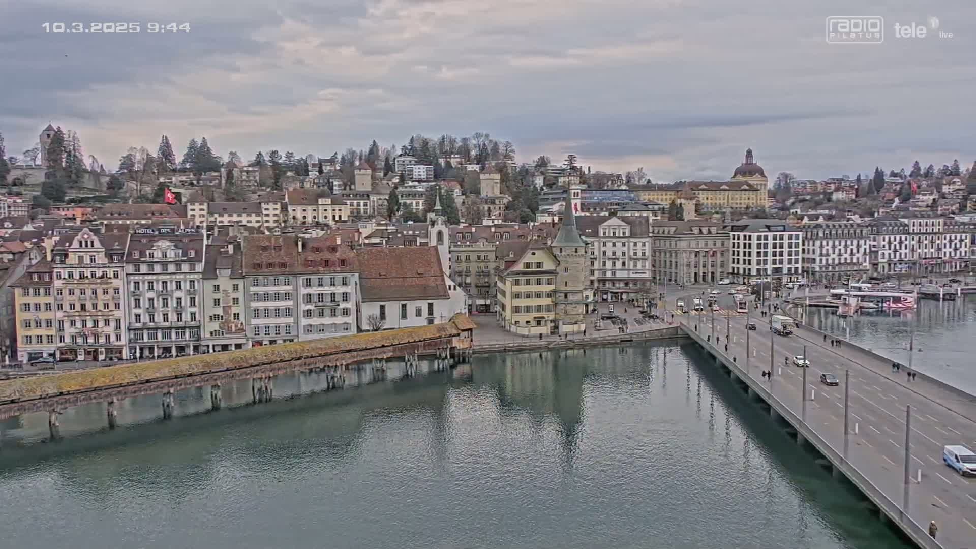 A European city with many buildings along a river under an overcast sky, a bridge crossing the river.