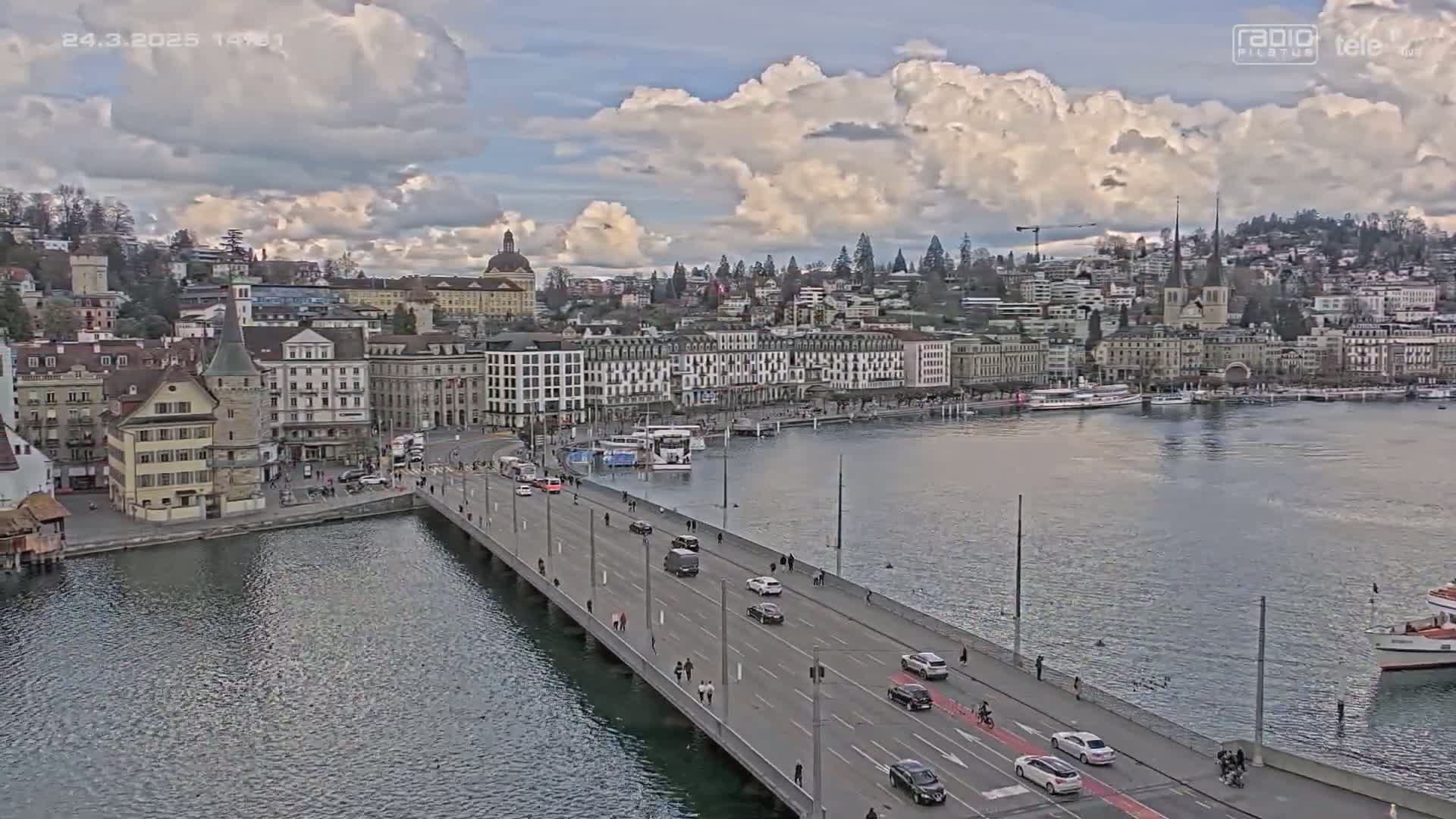 A bridge over a body of water with a city skyline in the background under a partly cloudy sky.