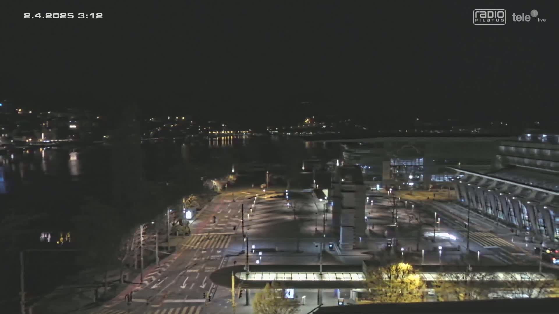 A nighttime view of a city waterfront with a large building and roadway, under clear skies.