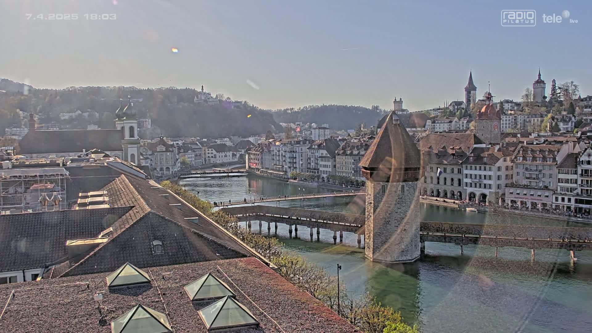 A picturesque cityscape with a covered bridge and water, under a sunny sky.