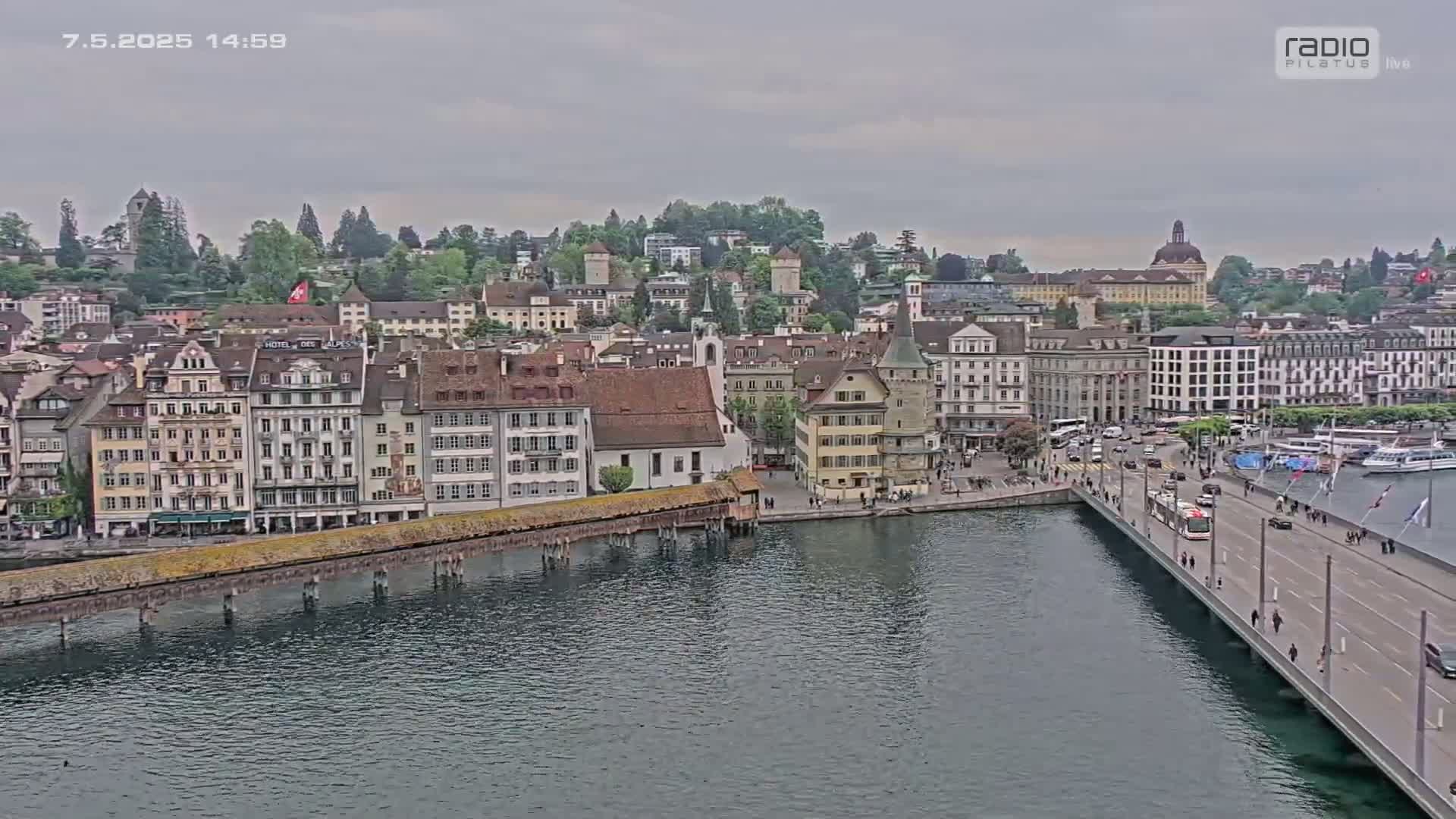 A city waterfront with many buildings, a bridge, and a calm body of water under an overcast sky.