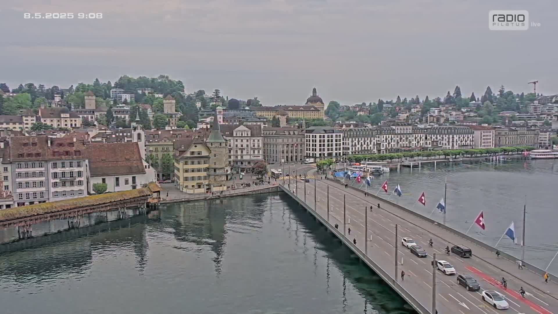 A bridge over a calm body of water leads to a city of historic European-style buildings under an overcast sky.
