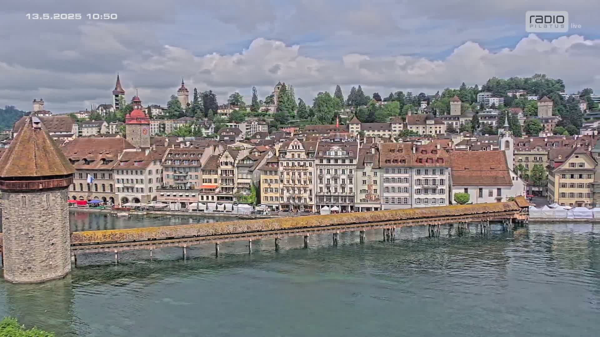 A stone bridge spans a calm body of water in front of a picturesque town with numerous buildings under a partly cloudy sky.
