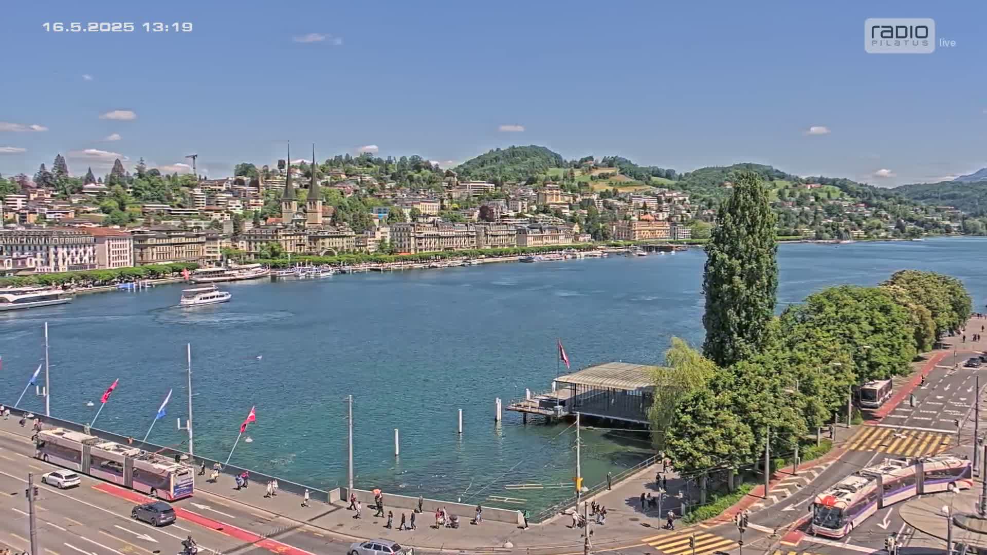 A sunny day overlooking a lake with a city waterfront, boats, and a roadway with trolleybuses.