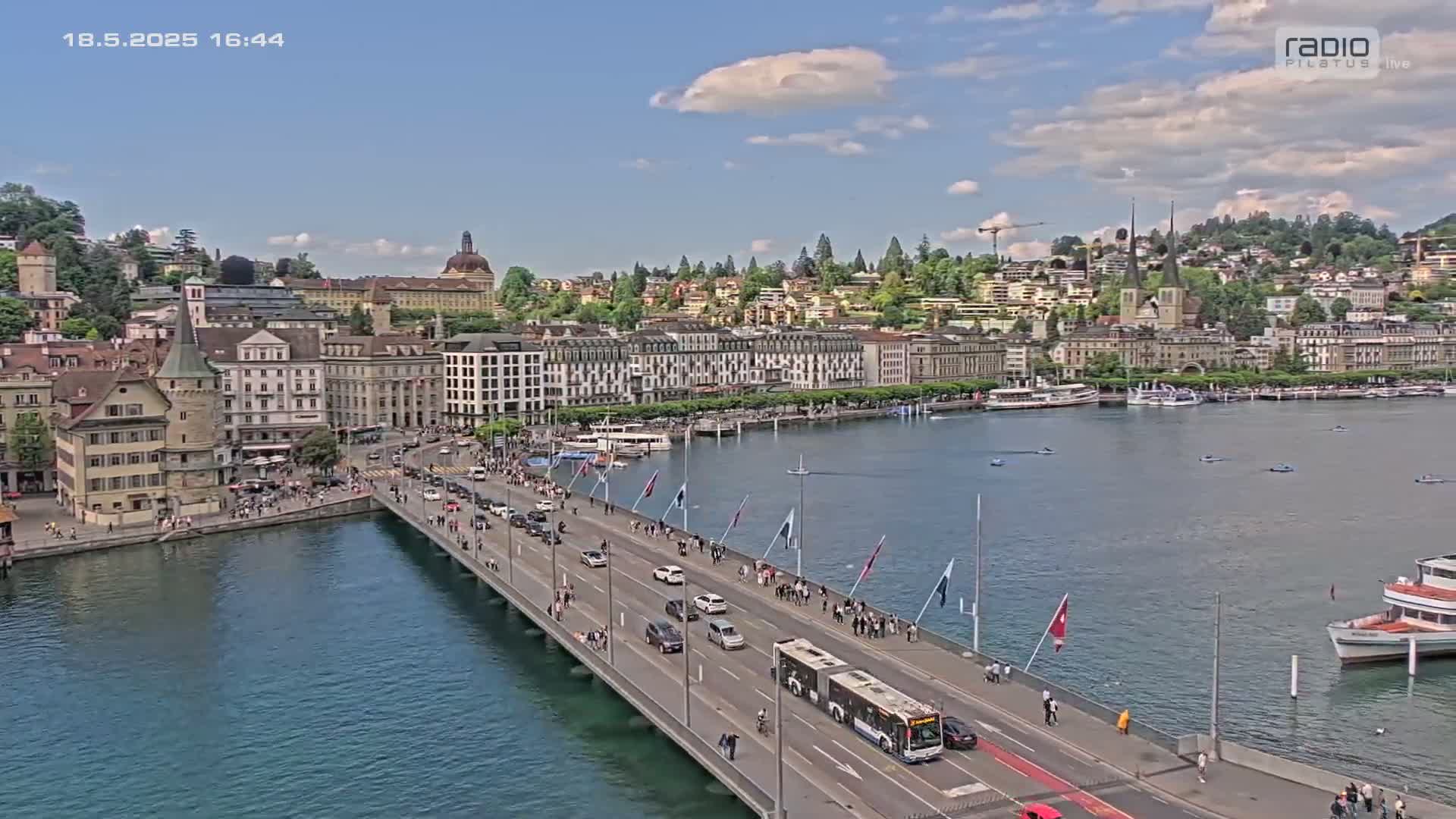 A bridge over a body of water with a city in the background on a partly cloudy day.
