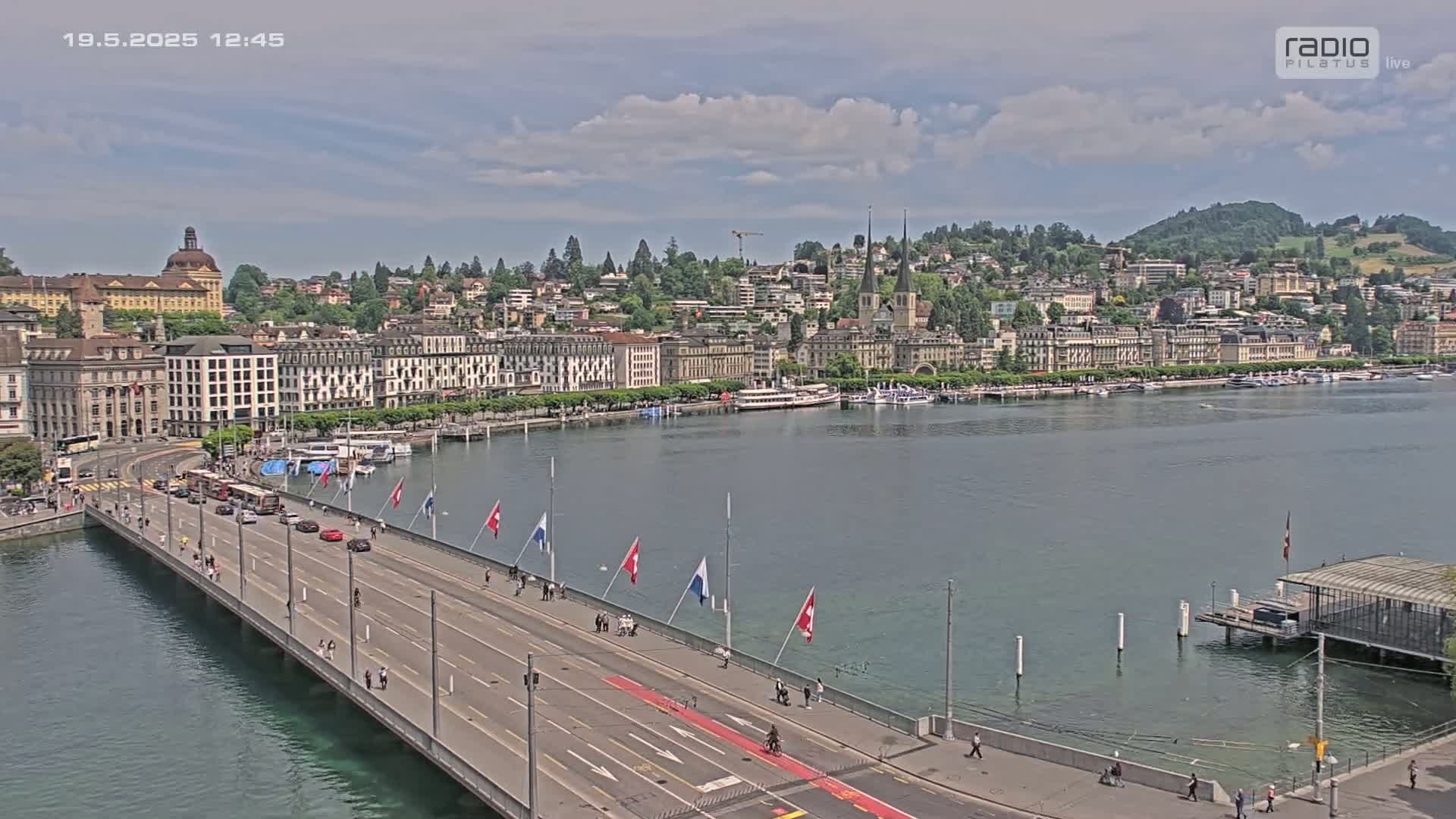 A long bridge extends over calm water toward a city skyline under a partly cloudy sky.