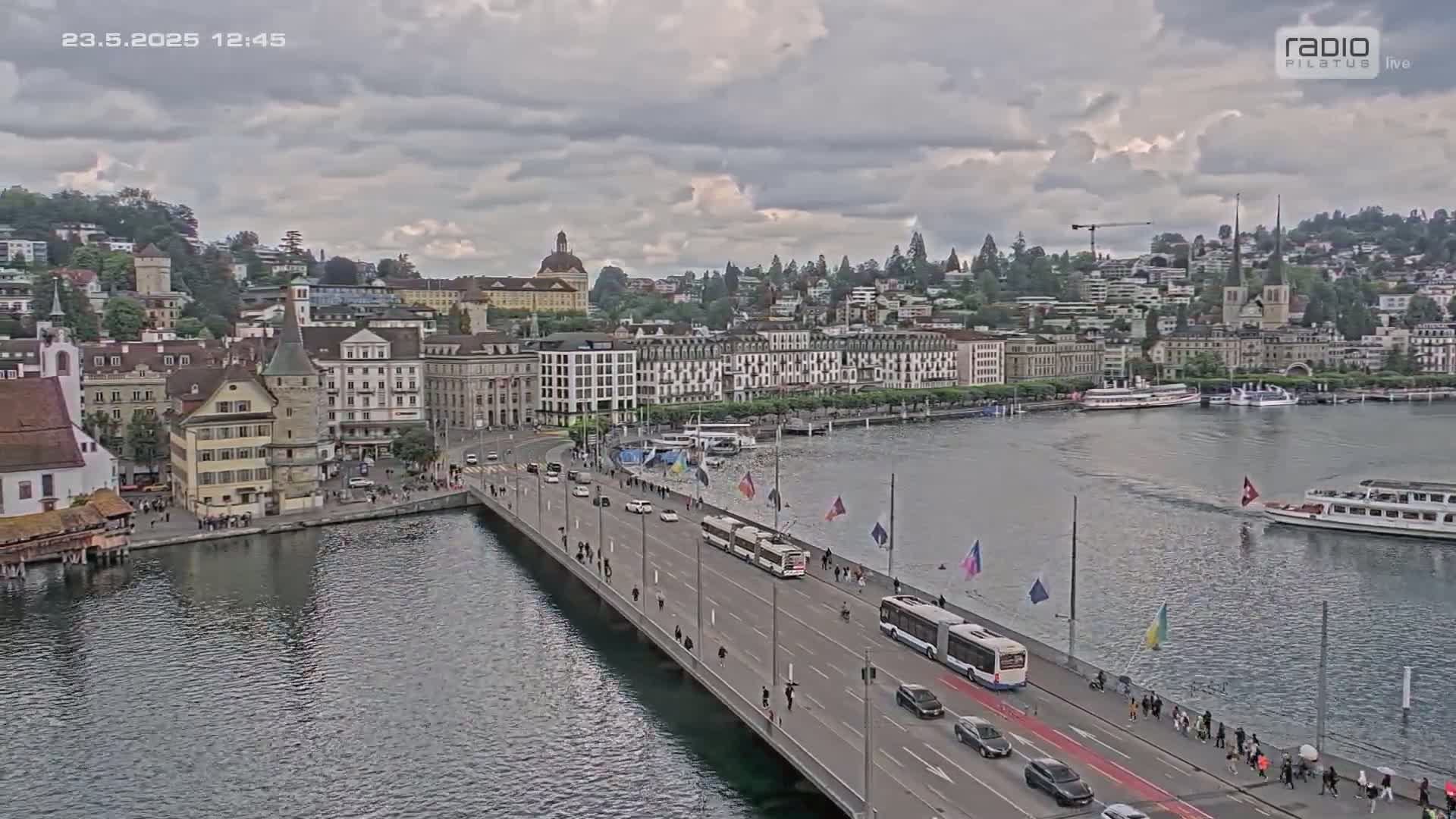 A bridge over a body of water leads to a city with many buildings under a cloudy sky.