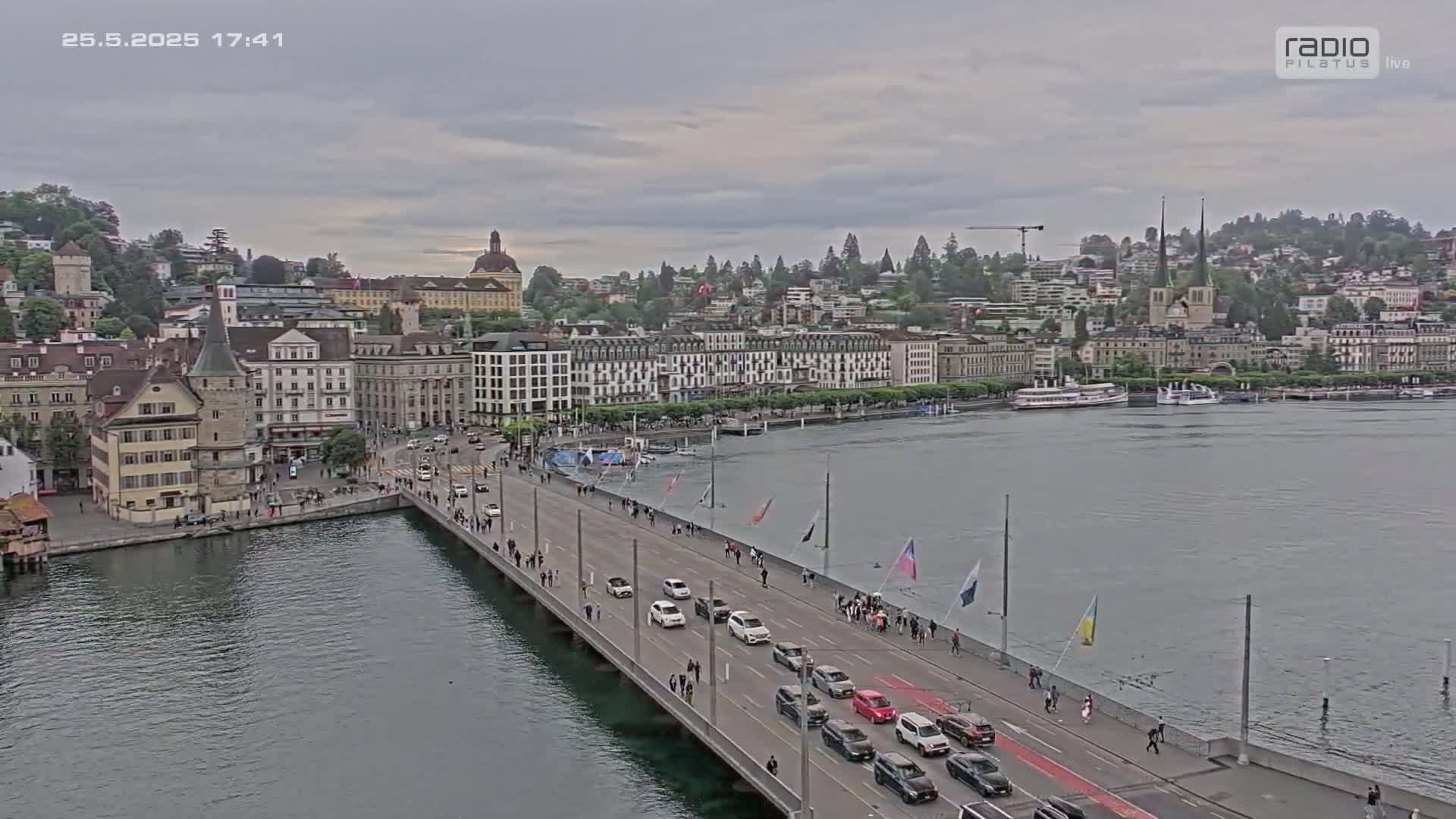 A bridge spans a body of water, with overcast skies overhead, showing a city with numerous buildings and boats in the distance.