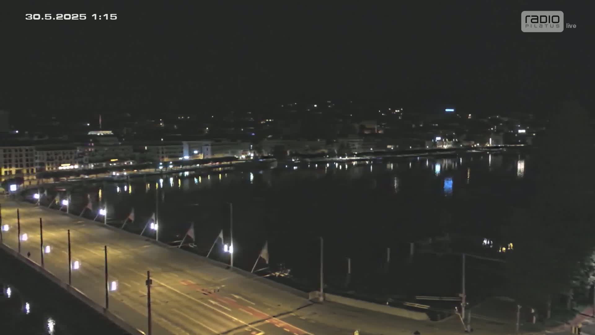 A nighttime view of a city's waterfront, showing a bridge with lights and calm water reflecting the city lights.