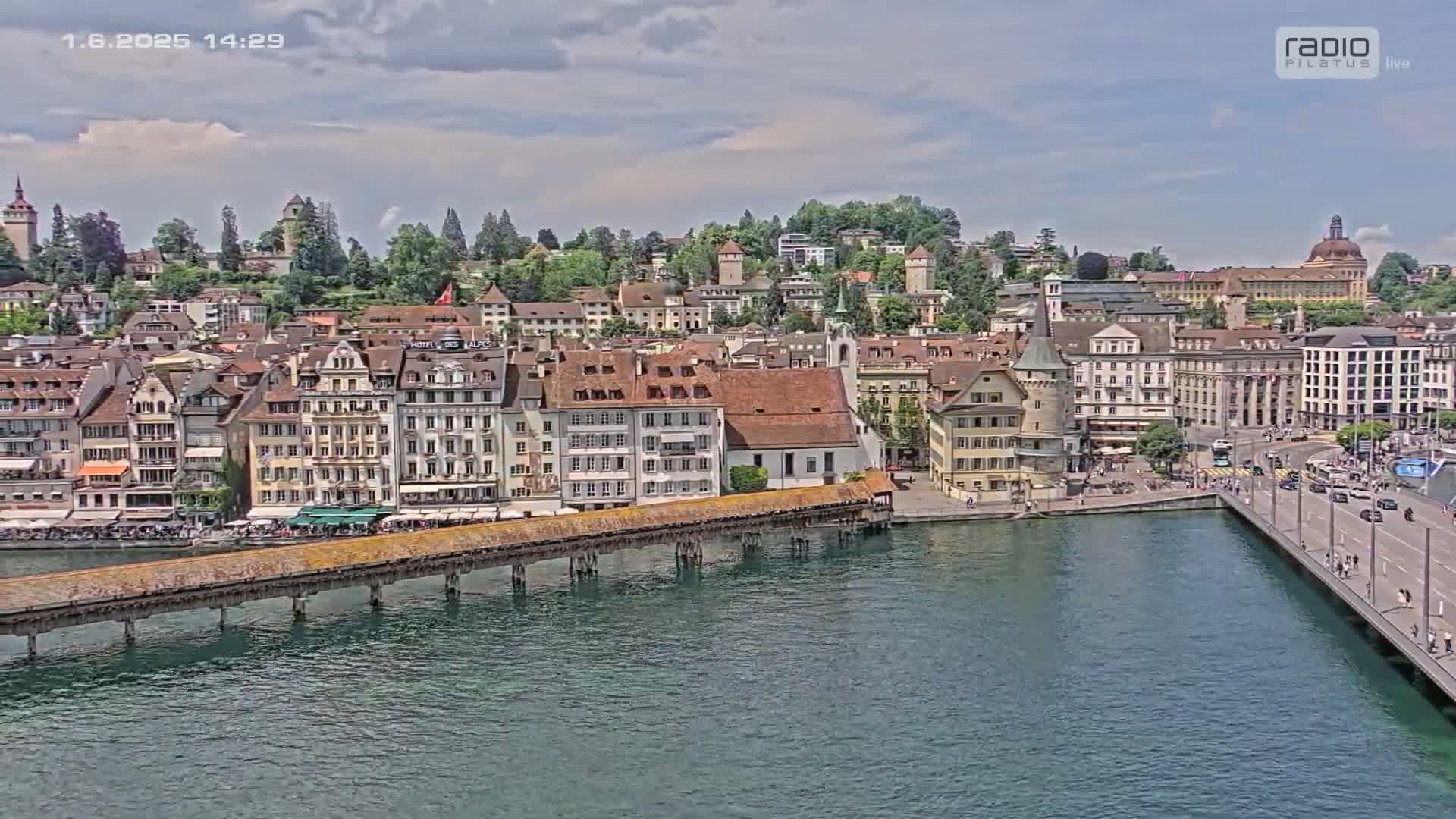 A picturesque European town with many buildings, a long wooden bridge over a body of water, and partly cloudy skies.