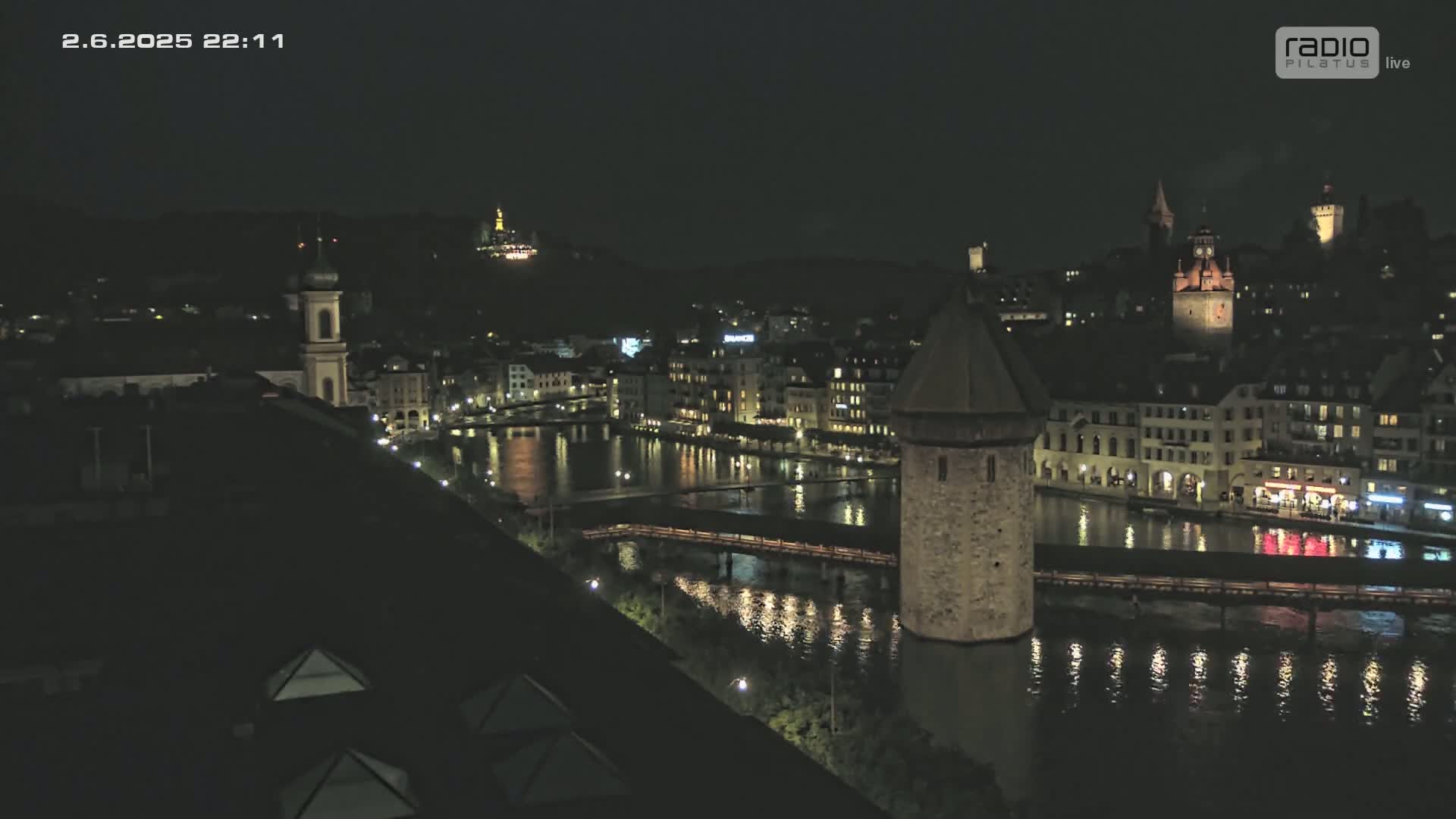 A nighttime view of a city with a river reflecting lights from buildings and a bridge, under a clear, dark sky.