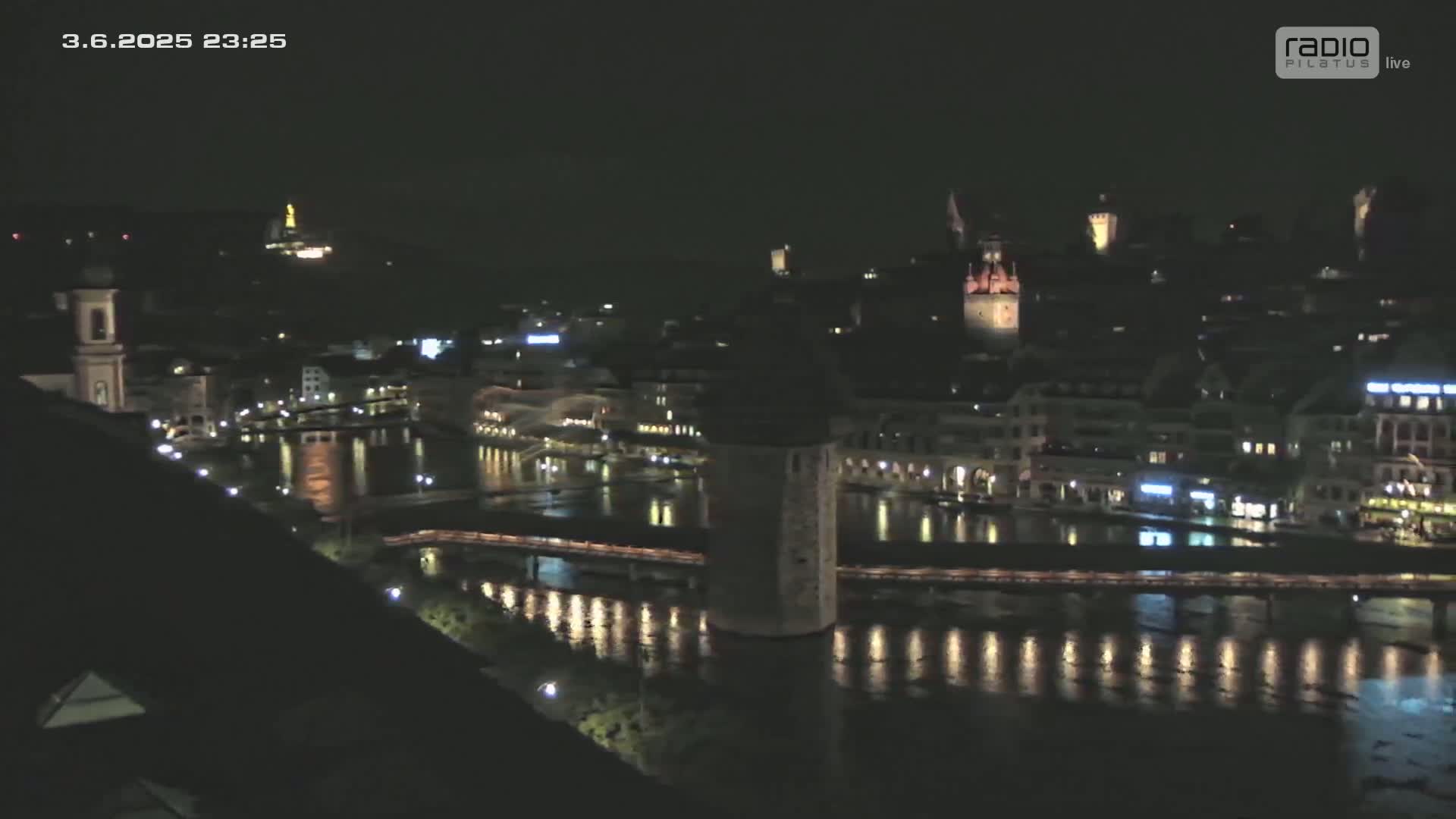 A nighttime, high-angle view of a city along a river, illuminated by lights reflecting on the water.
