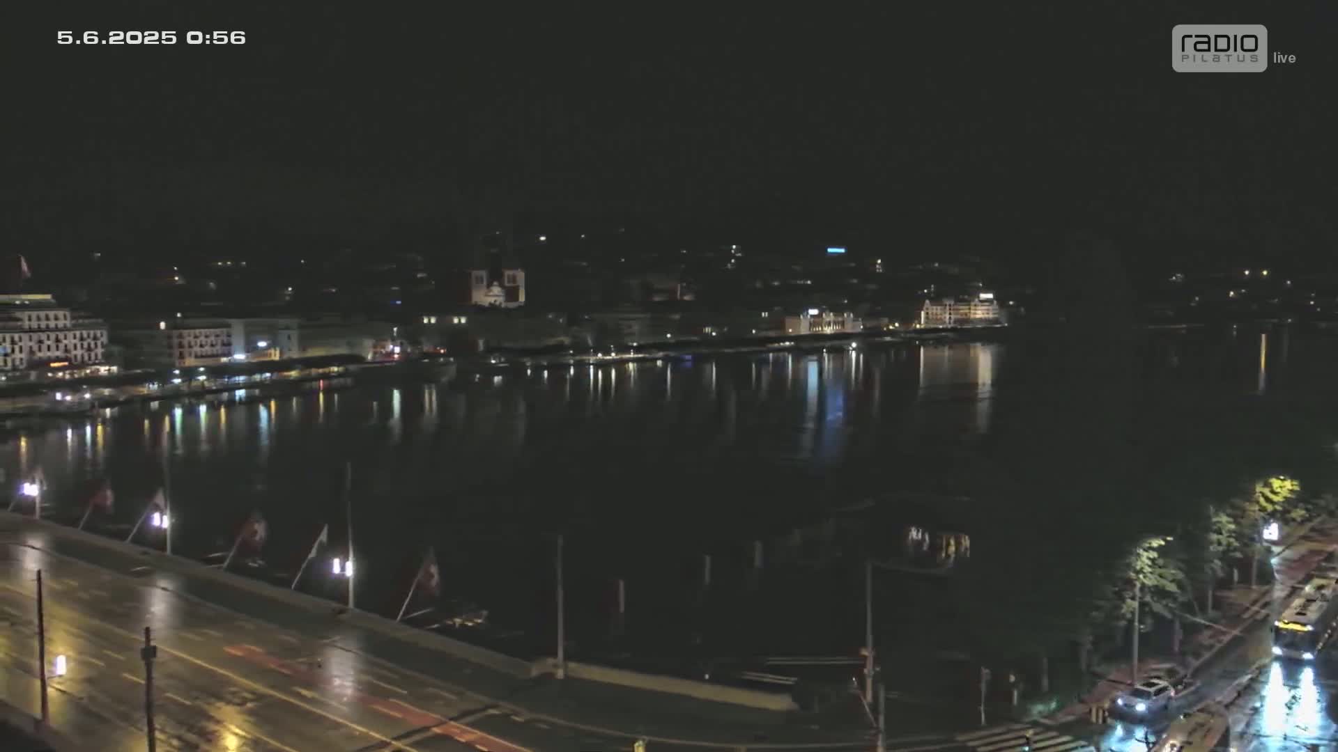 A nighttime view of a city waterfront, showing a calm body of water reflecting city lights under a dark, possibly rainy sky.