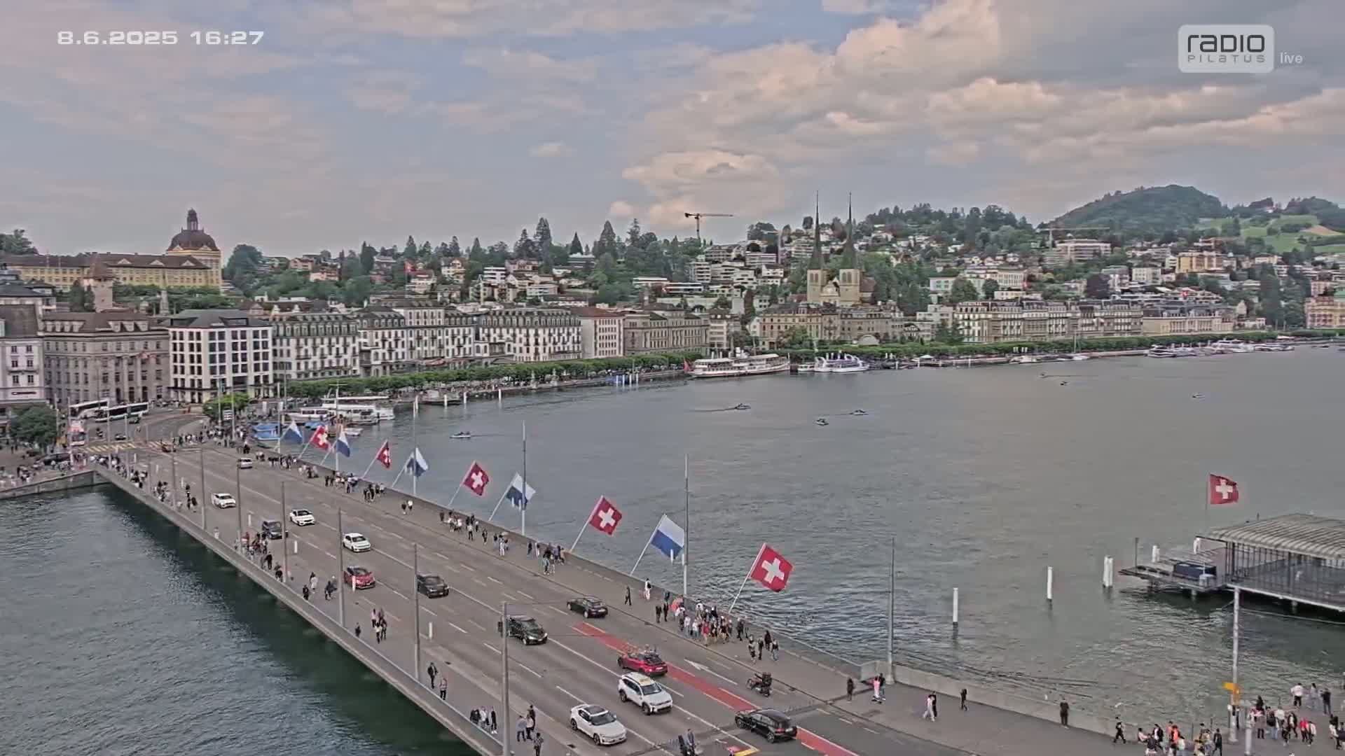 A long bridge with cars and pedestrians on it stretches across a body of water towards a city under a partly cloudy sky.