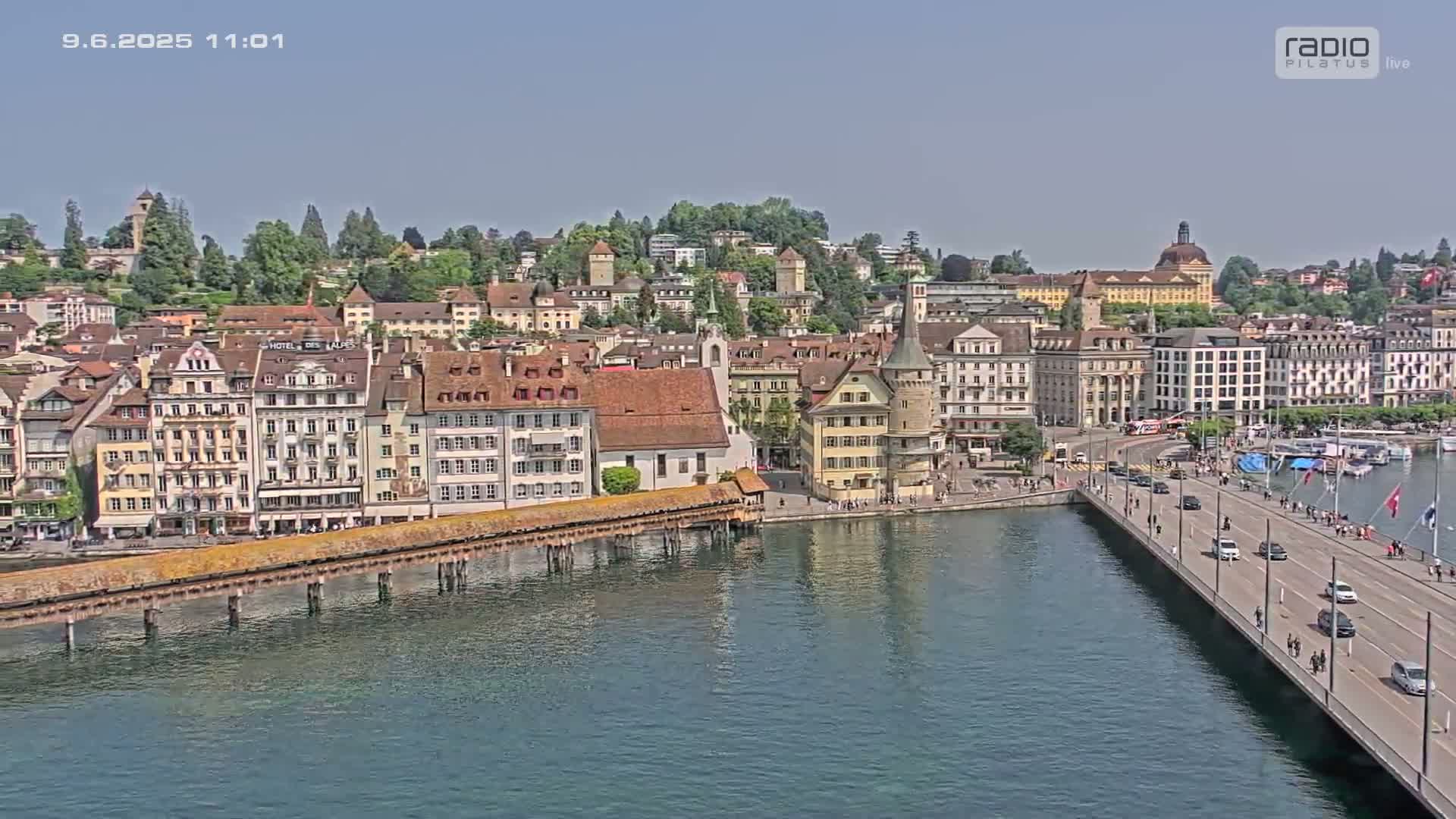 A picturesque waterfront town with numerous buildings, a covered bridge, and a roadway bridge over calm water under a clear sky.