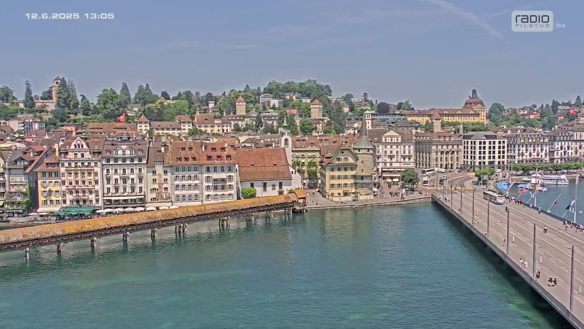 A picturesque waterfront town with colorful buildings, a covered bridge, and a modern bridge, all under a clear sunny sky.