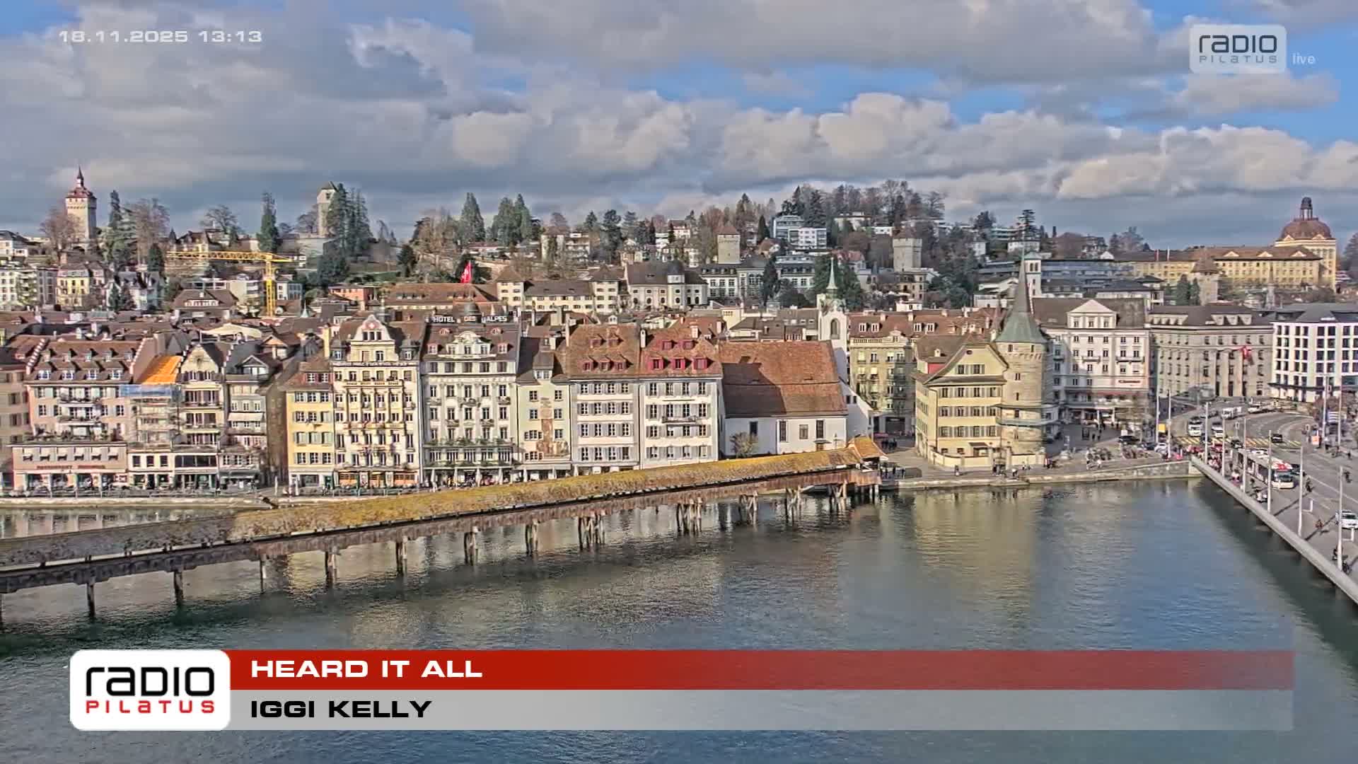 A clear night view captures a city waterfront with lights reflecting on calm water, an illuminated street featuring buses and pedestrians in the foreground, and a distant urban skyline.