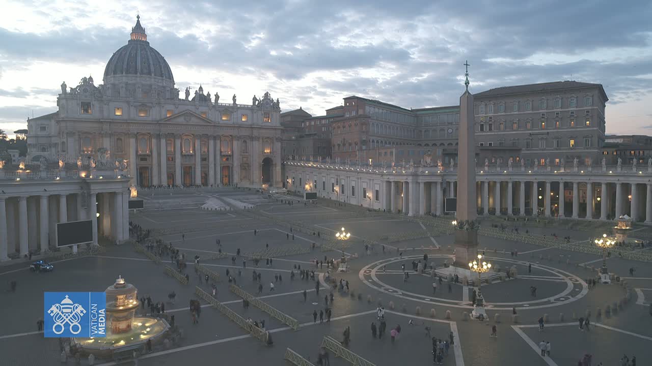 St. Peter's Basilica and St. Peter's Square in Vatican City at dusk, with a few people scattered across the large plaza.