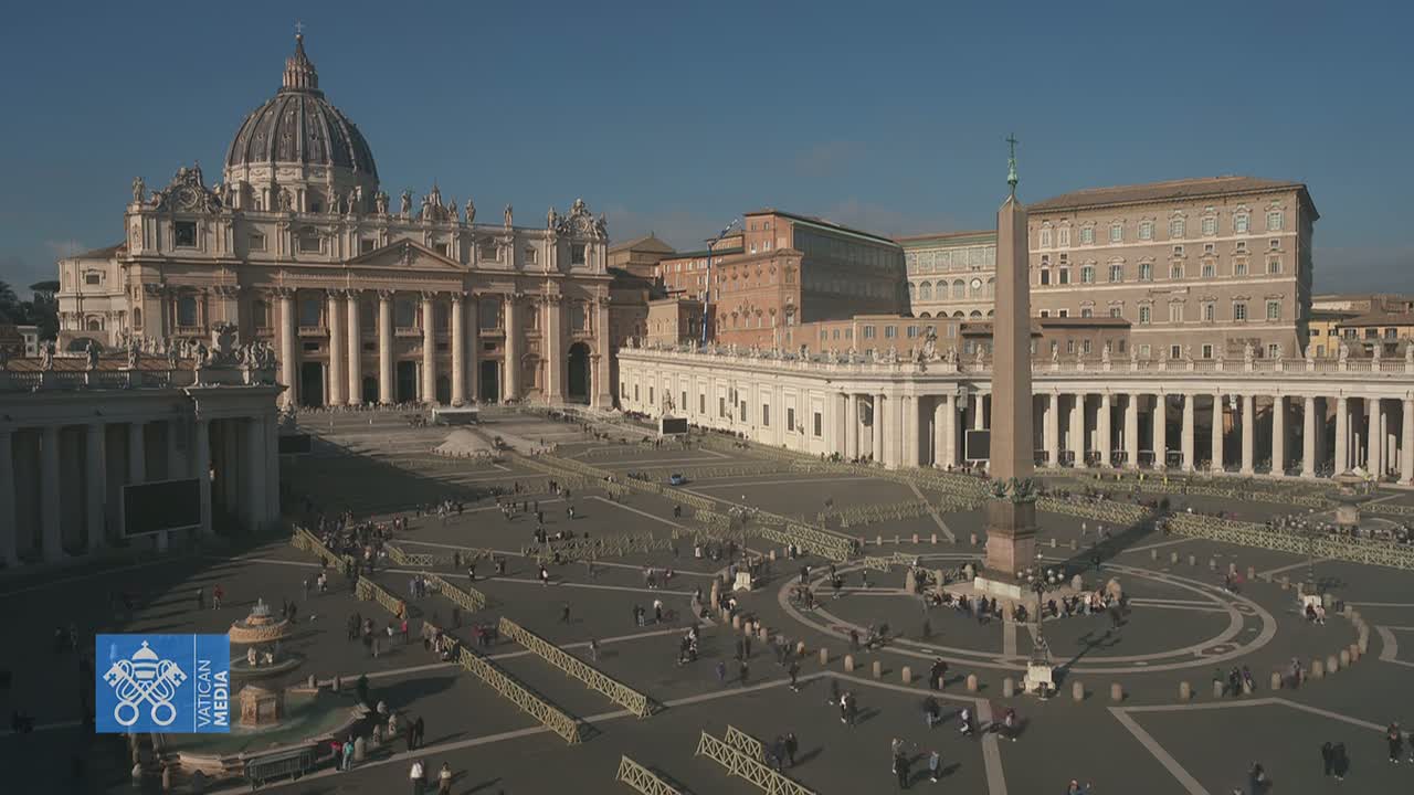 A large plaza with St. Peter's Basilica in the background on a sunny day, populated by a scattering of people and marked by barriers.