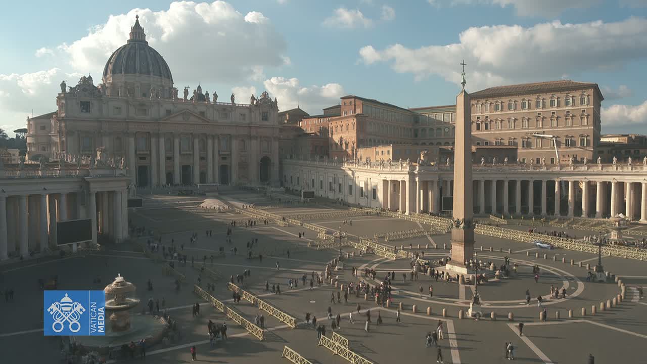 St. Peter's Square in Vatican City, under a partly cloudy sky, is filled with people scattered across the large plaza, surrounded by classical architecture.