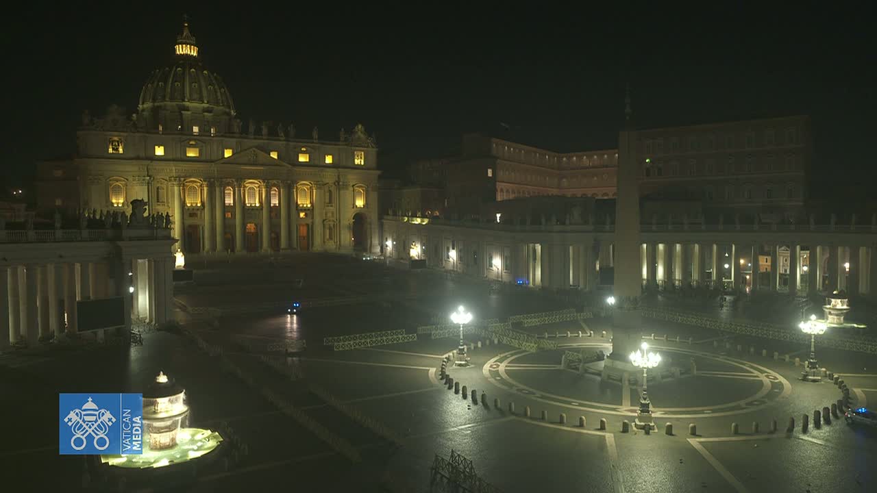 St. Peter's Basilica and Square are illuminated at night, with a mostly empty plaza and wet pavement.