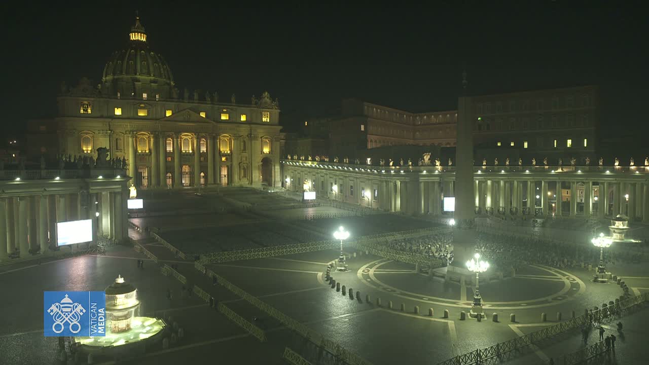 St. Peter's Basilica and Square at night, illuminated, with a sparse crowd gathered in the plaza.