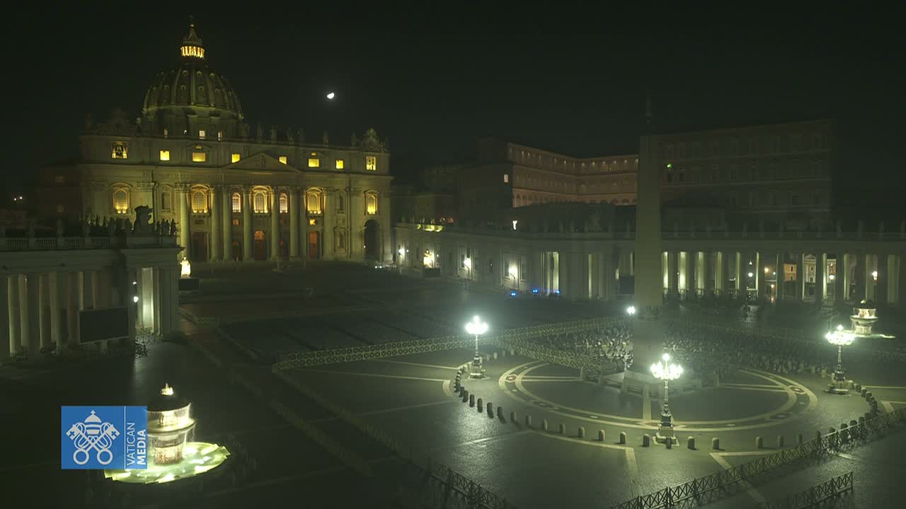 St. Peter's Basilica and Square at night, illuminated under a partly cloudy sky with a visible moon.