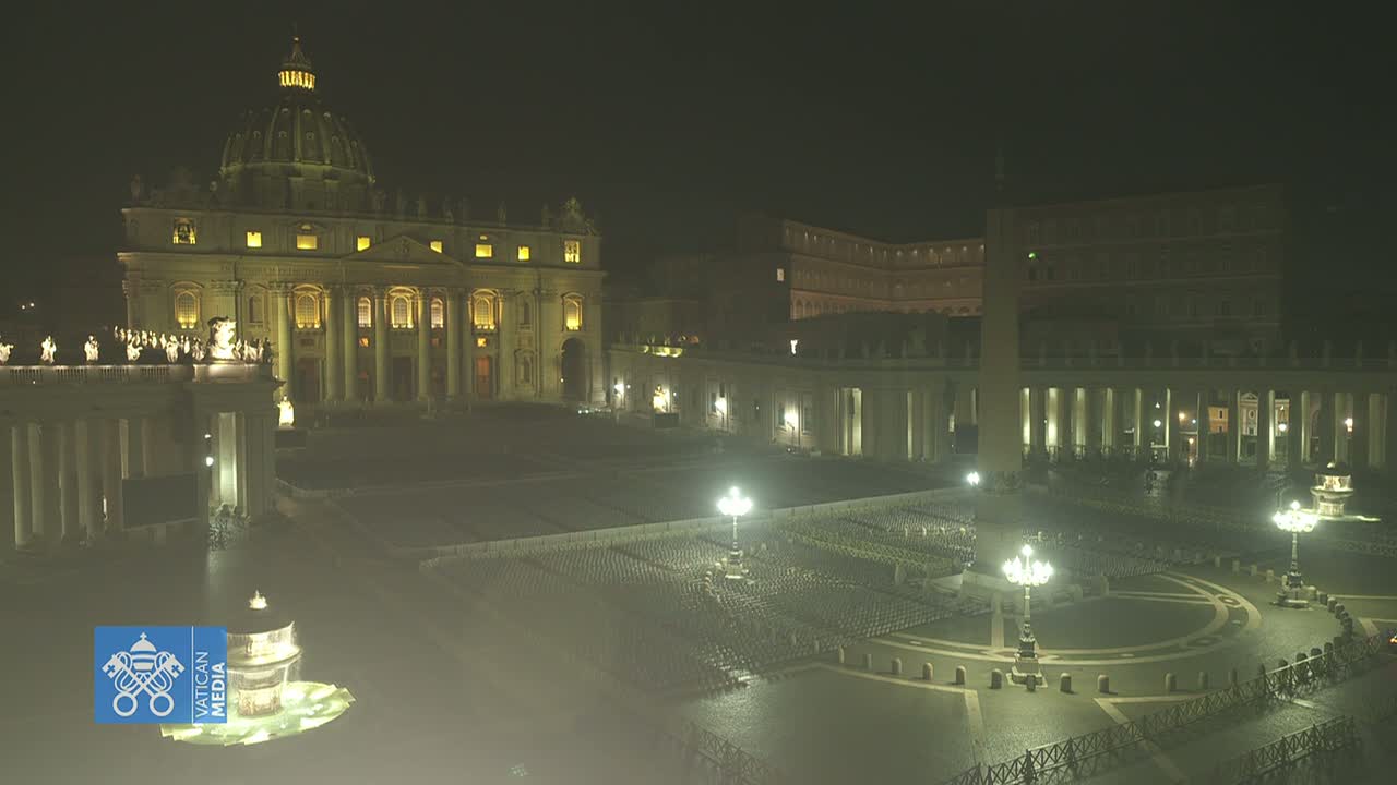 St. Peter's Basilica and St. Peter's Square at night, illuminated, with empty chairs arranged in the square under a hazy sky.