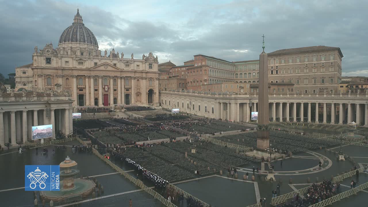 St. Peter's Square in Vatican City, under a cloudy sky, is filled with many people seated in rows of chairs facing St. Peter's Basilica.