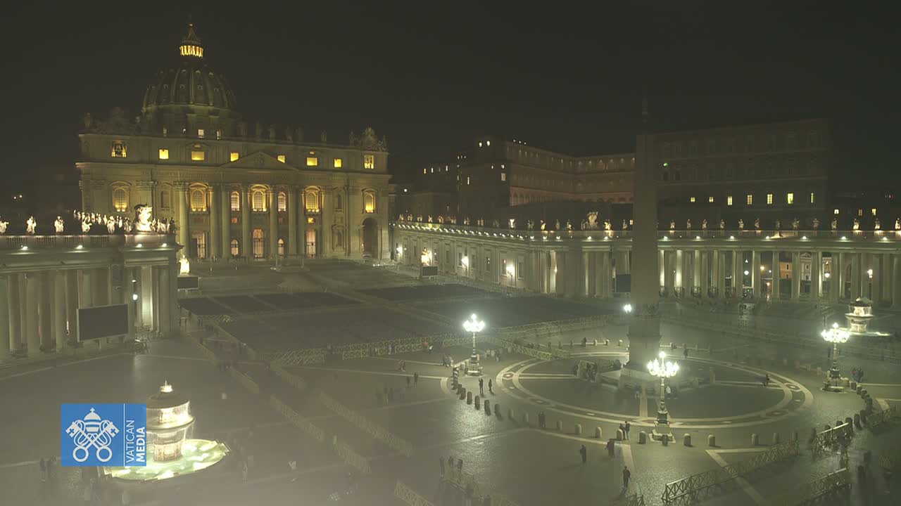 St. Peter's Basilica and Square are illuminated at night, with a few people present in the large plaza.