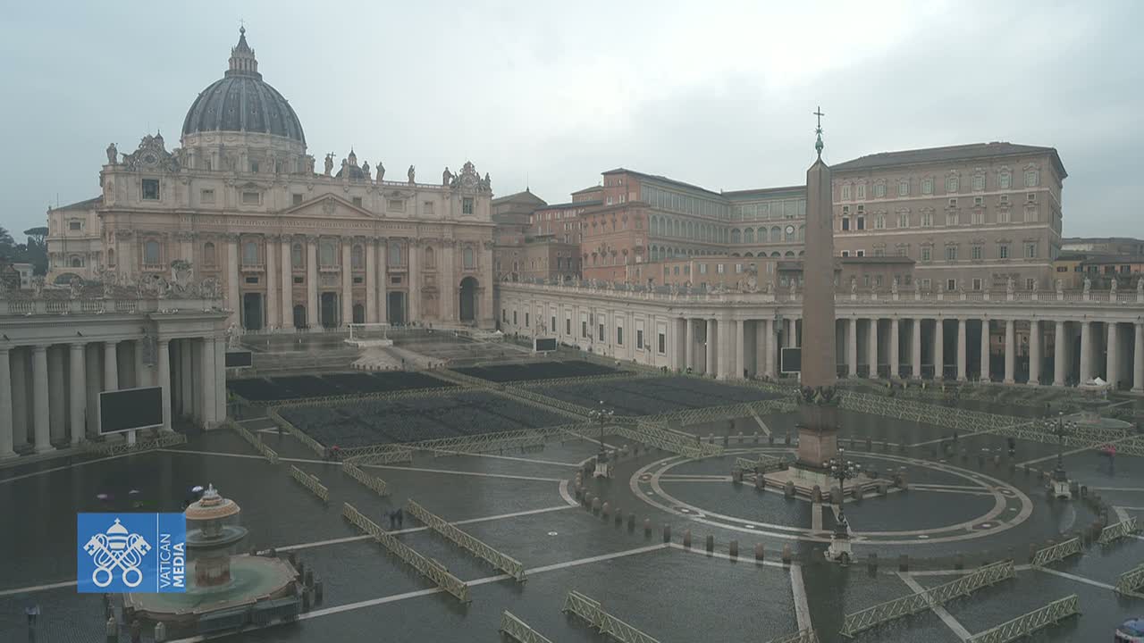 St. Peter's Square in Vatican City on an overcast day, showing the Basilica and surrounding colonnades, with the square largely empty and wet.